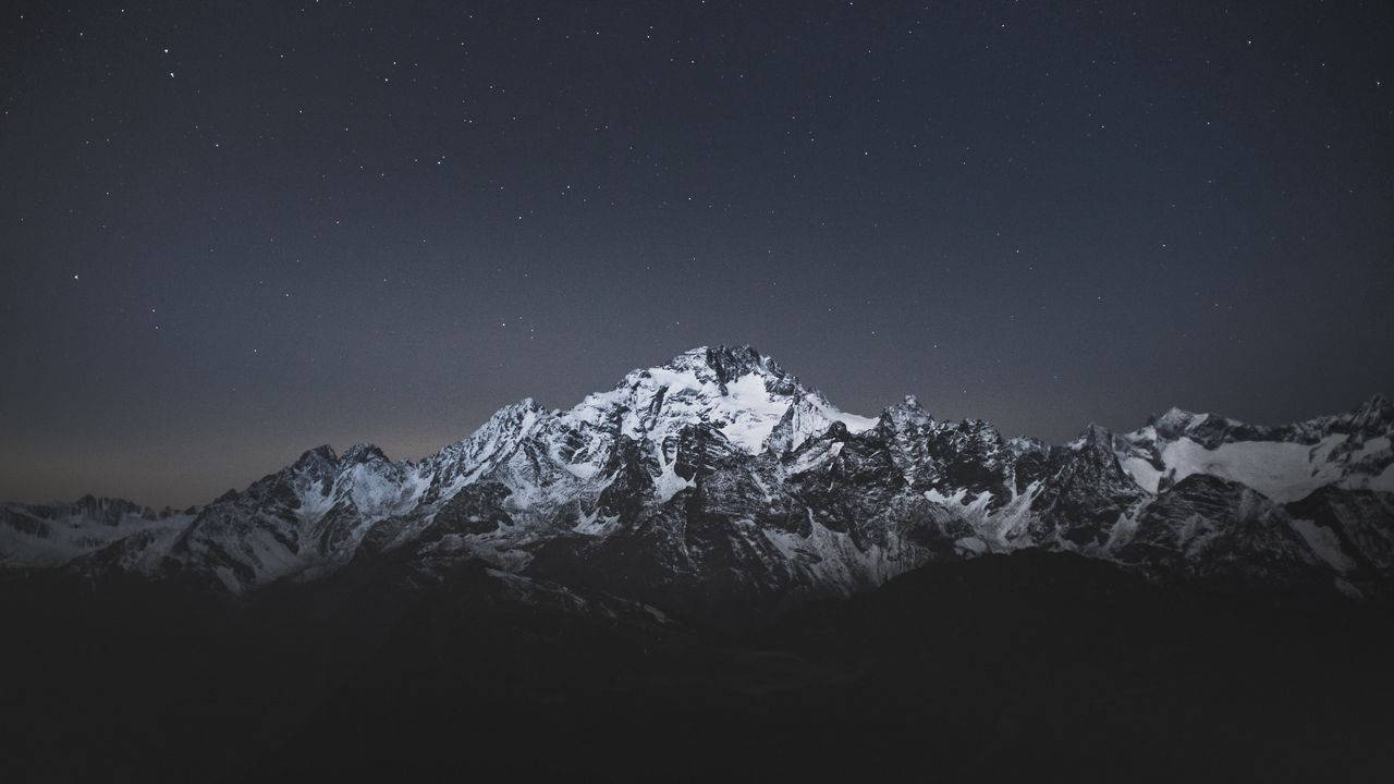 Stand Tall And Admire The Beauty Of The Night Sky And A Majestic Mountain. Background