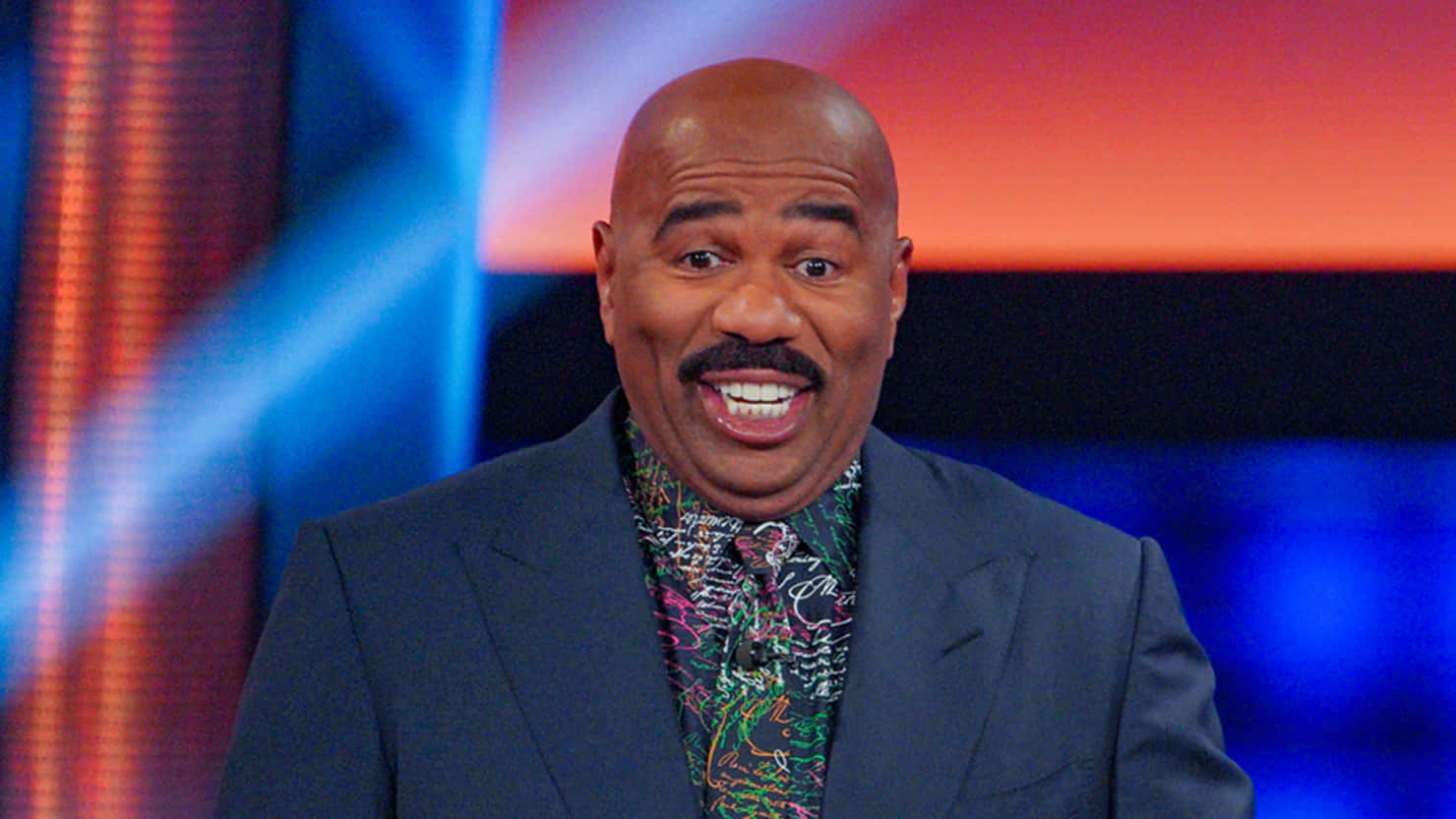 Steve Harvey Smiling In A Colorful Shirt Background