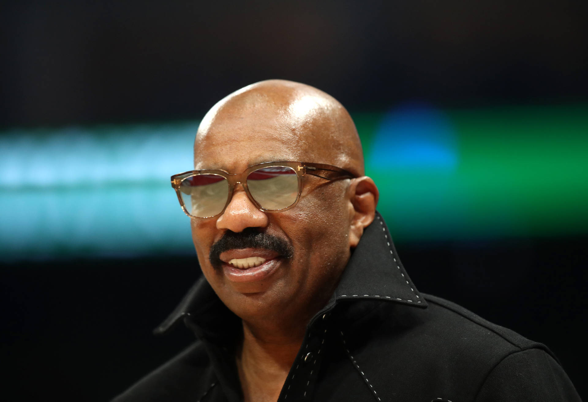 Steve Harvey Smiling In Coat And Sunglasses Background