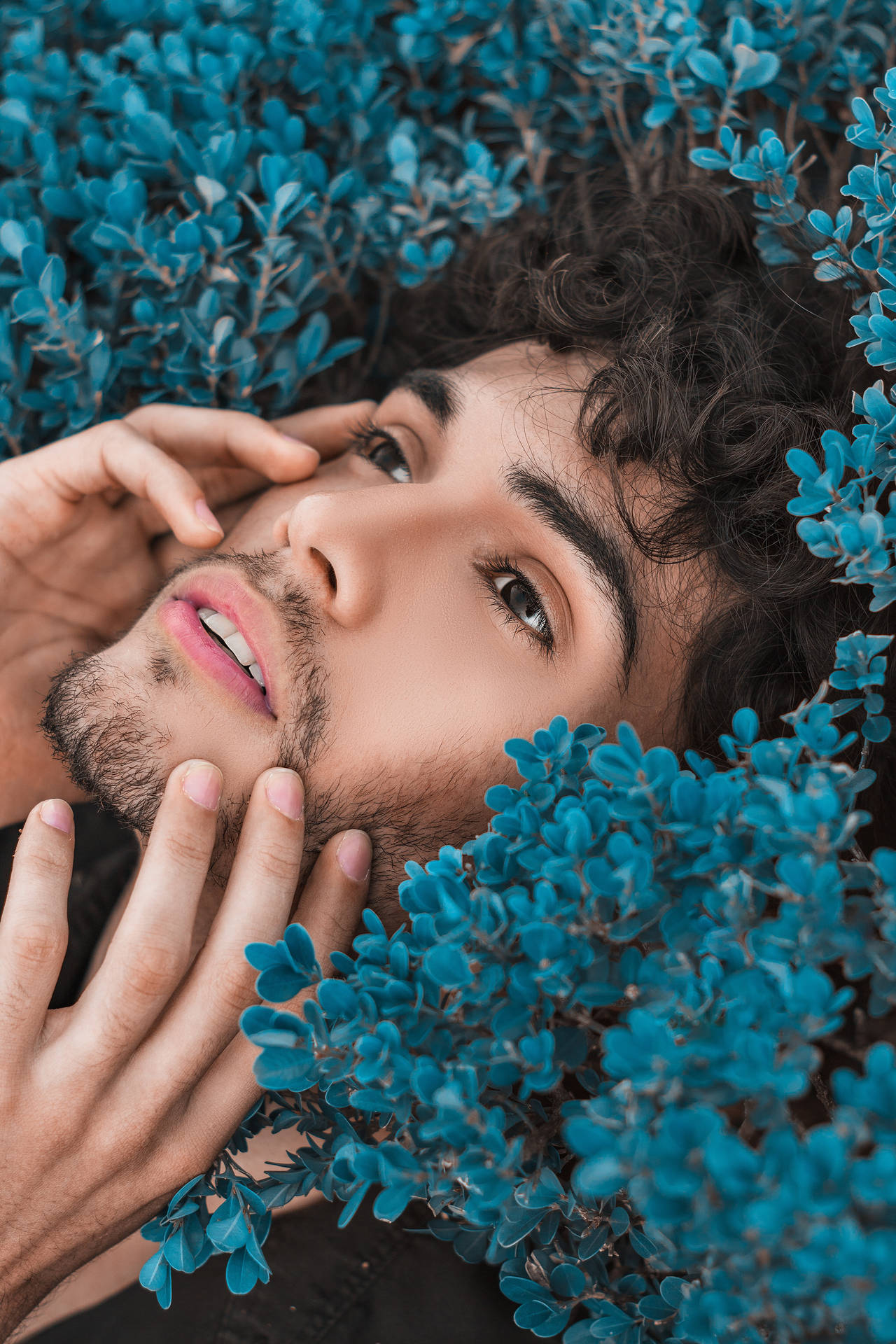 Stylish Man In Dynamic Blue Pose Amidst Foliage Background