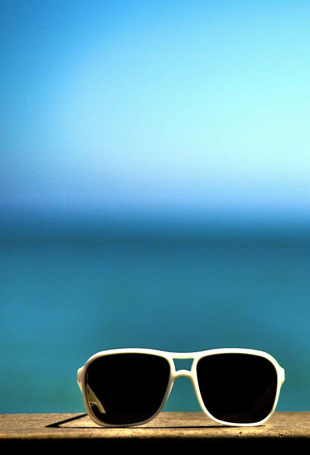 Sunglasses On A Wooden Table With The Ocean In The Background Background