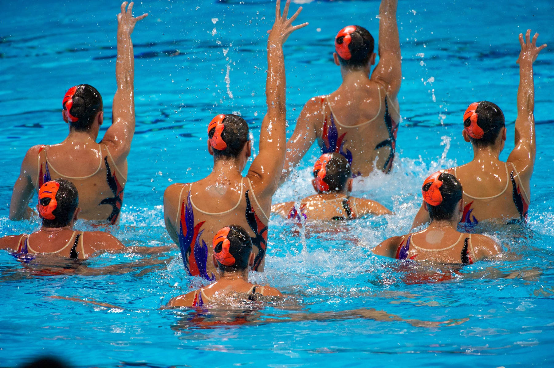 Synchronized Swimmers With Hands Up In Perfect Harmony Background