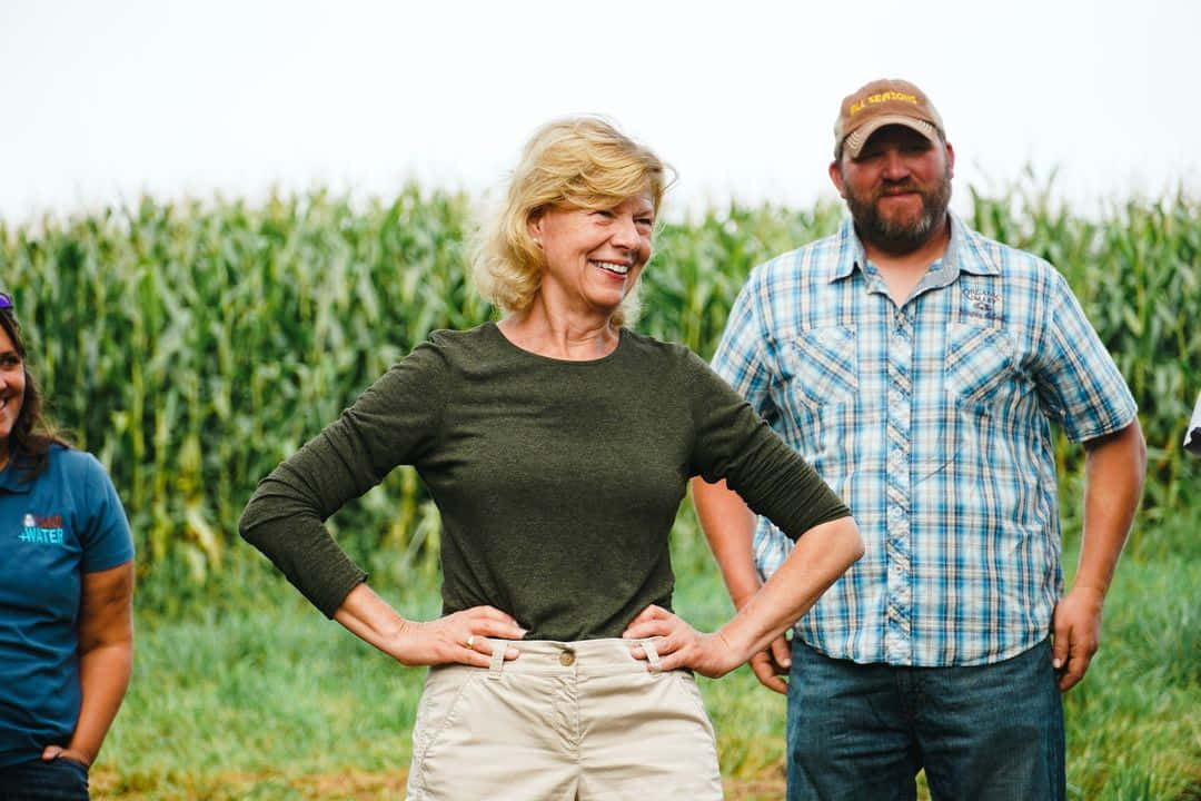 Tammy Baldwin Standing In A Cornfield Background