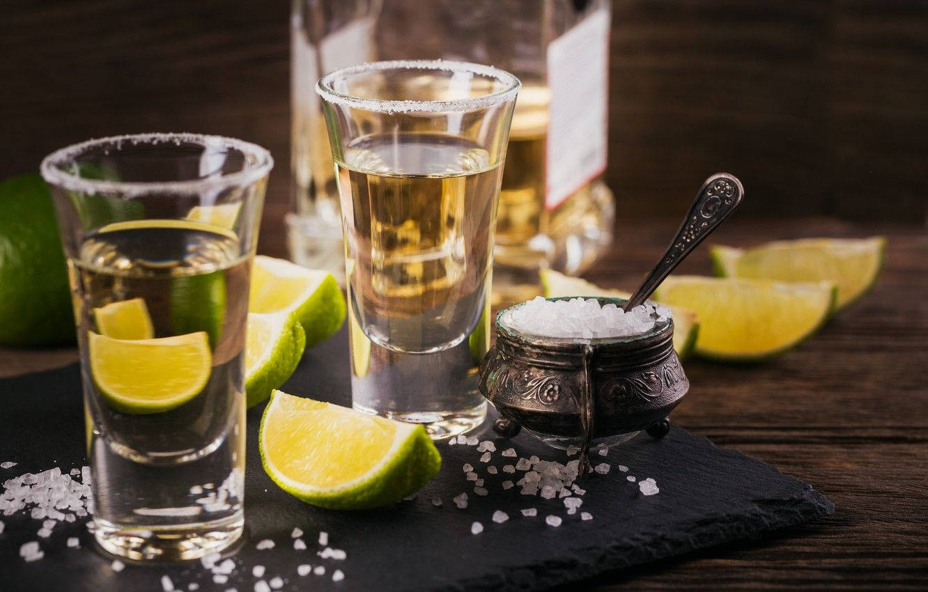 Tequila On Shot Glasses With Lime Slices Background