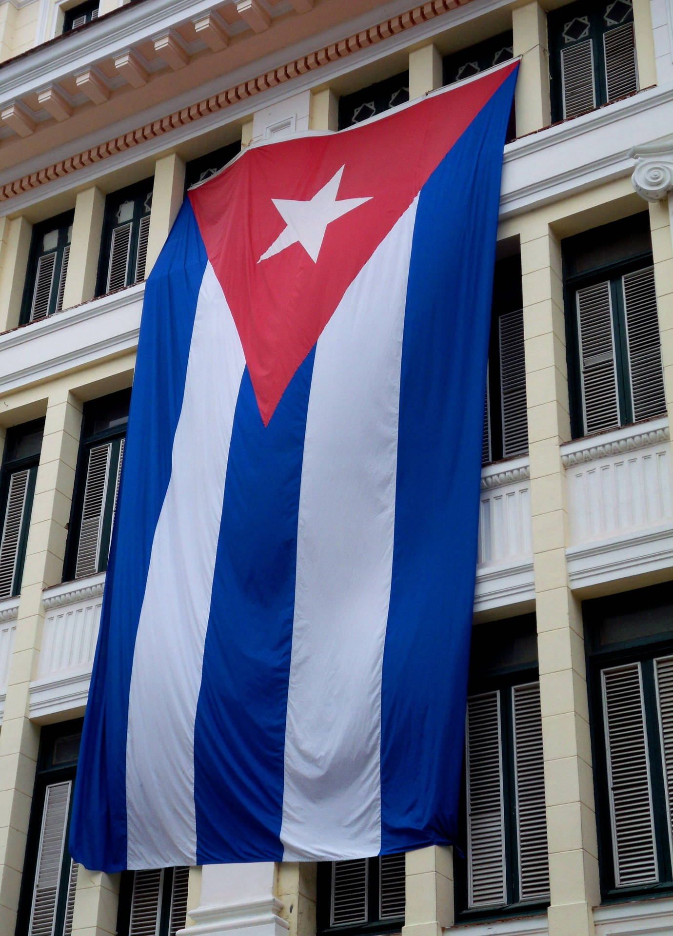 The Authentic Cuban Flag Waving In Front Of A Classical Cuban Building. Background