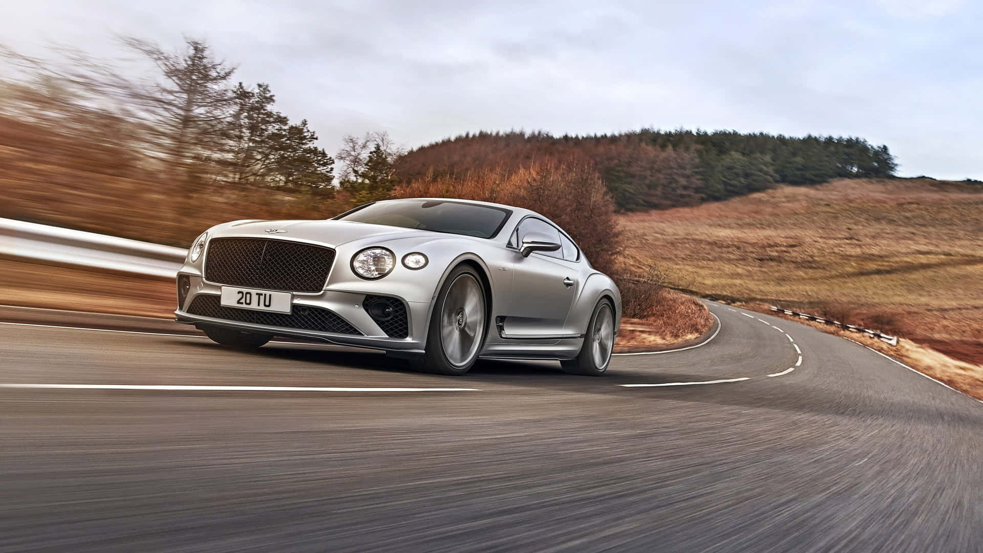 The Bentley Continental Gt Is Driving Down A Road Background