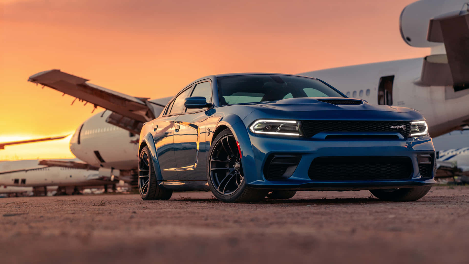 The Blue Dodge Charger Parked In Front Of An Airplane Background