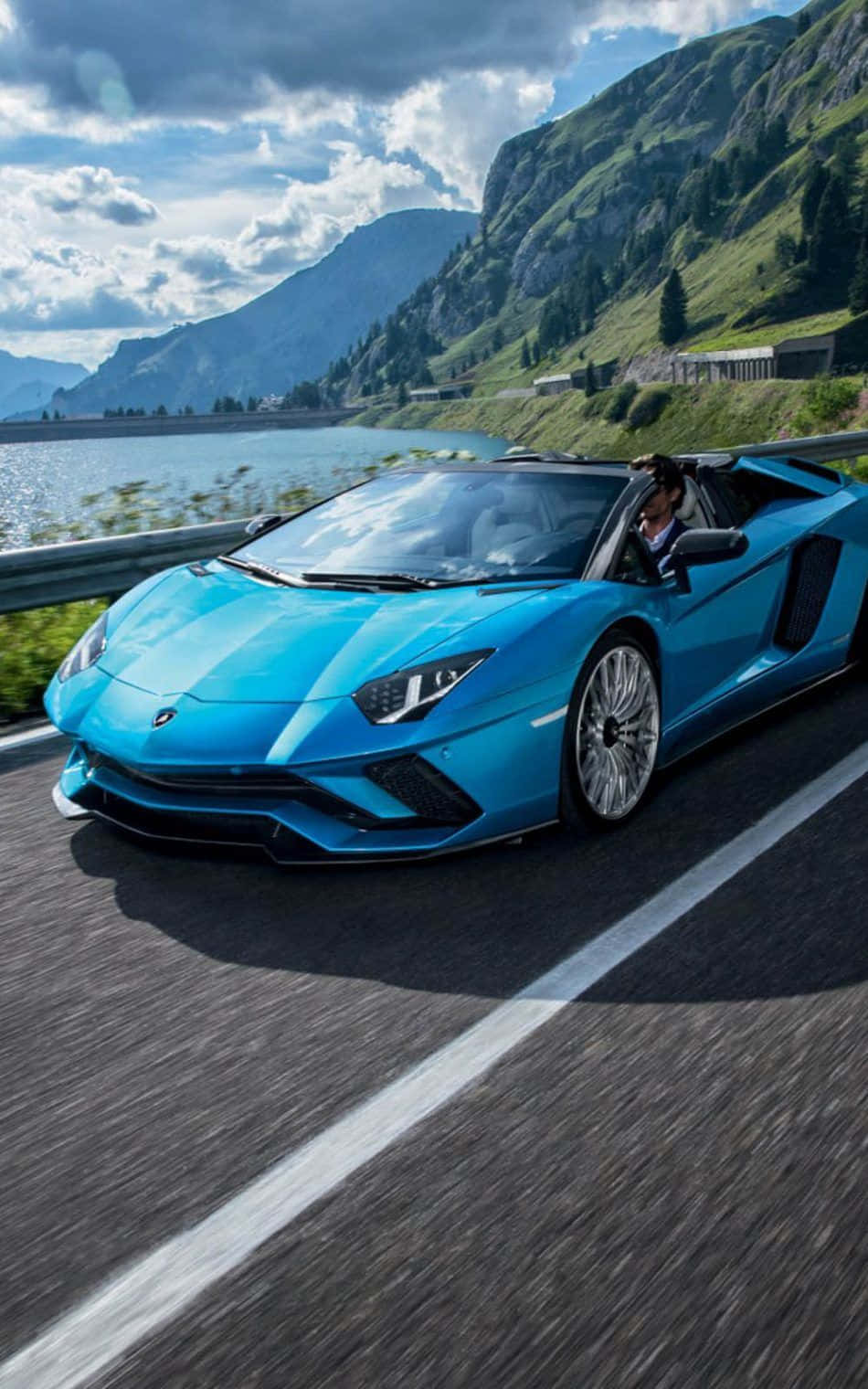 The Blue Lamborghini Spyder Is Driving Down The Road