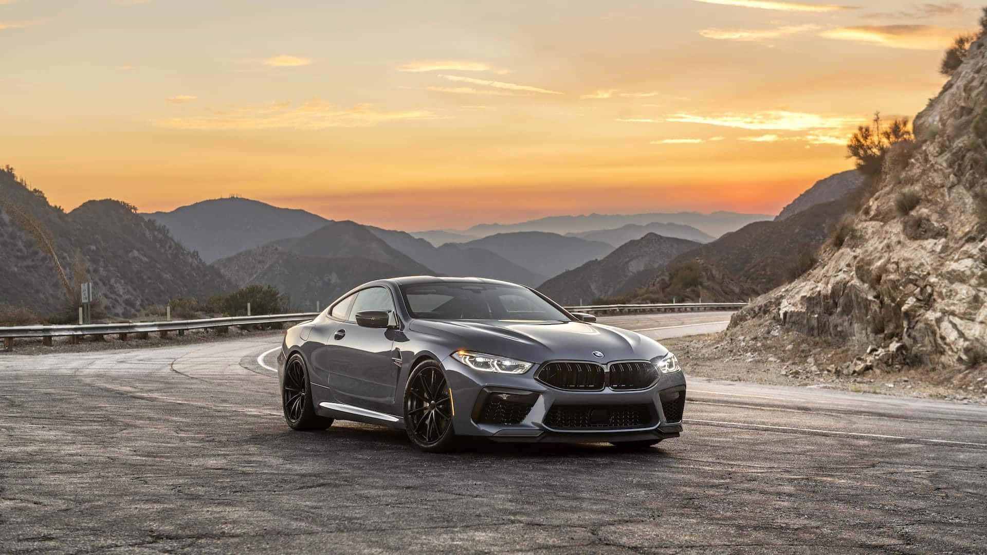 The Bmw M8 Is Driving Down A Mountain Road At Sunset