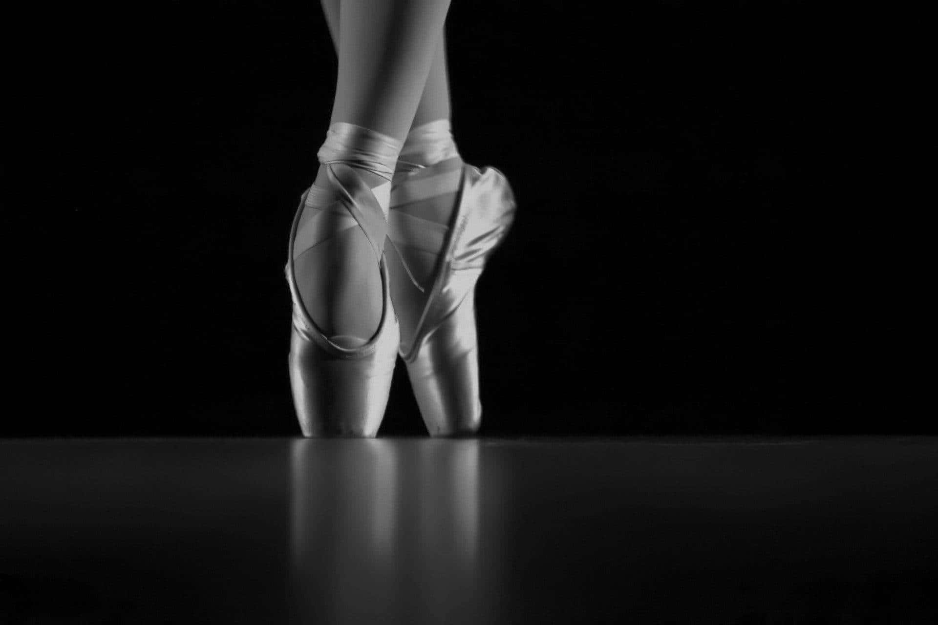 The Elegance Of Ballet: Gleaming Pointe Shoes In The Darkness Background