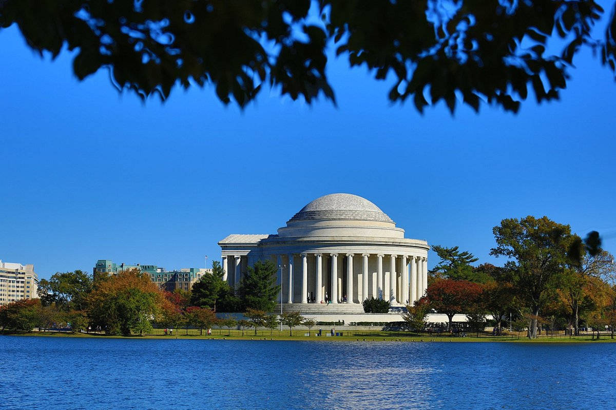 The Jefferson Memorial Standing Majestic Against The Blue Sky And Shimmering River