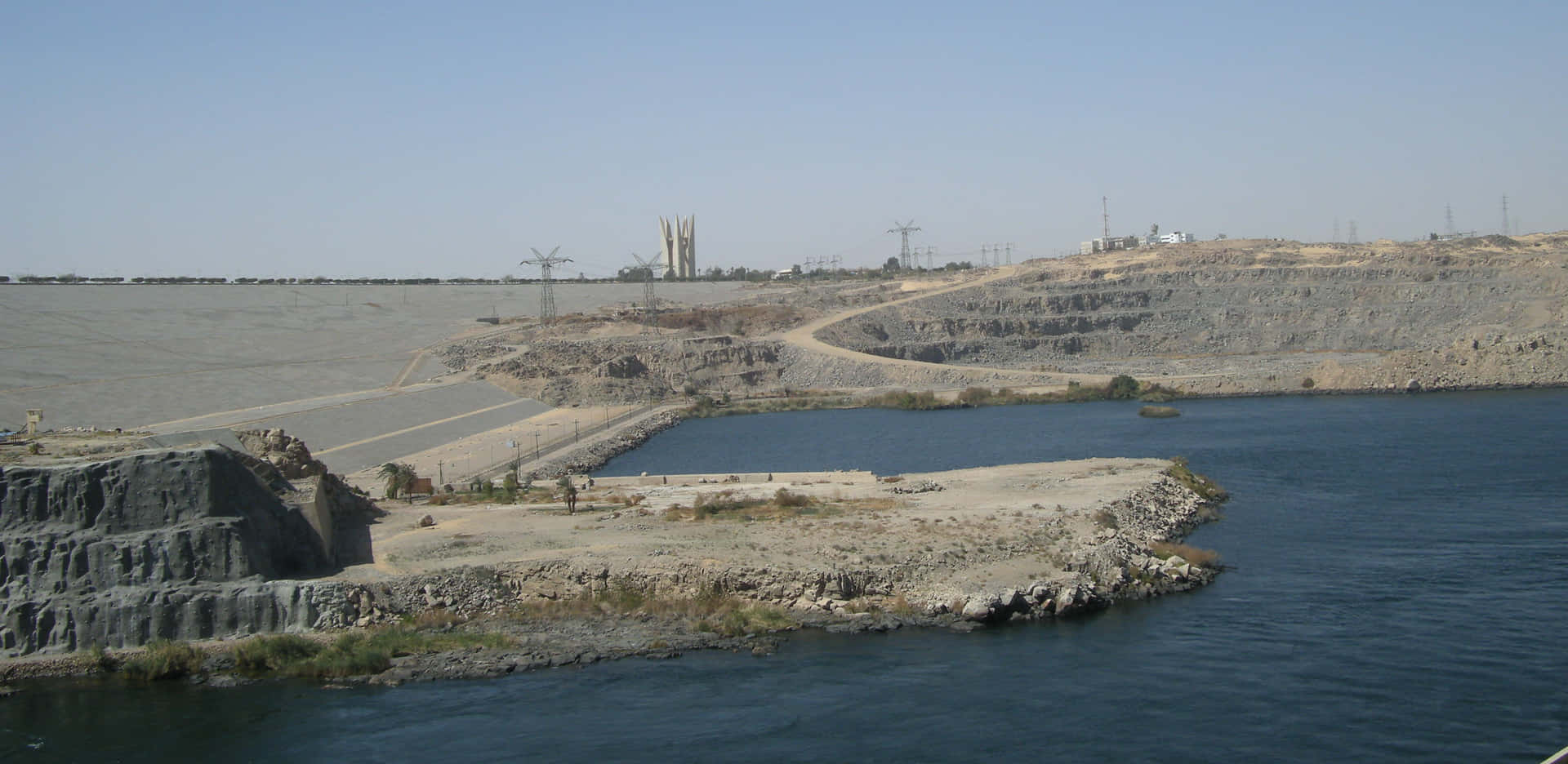 The Majestic Aswan High Dam Overlooking The Breathtaking Desert River Background