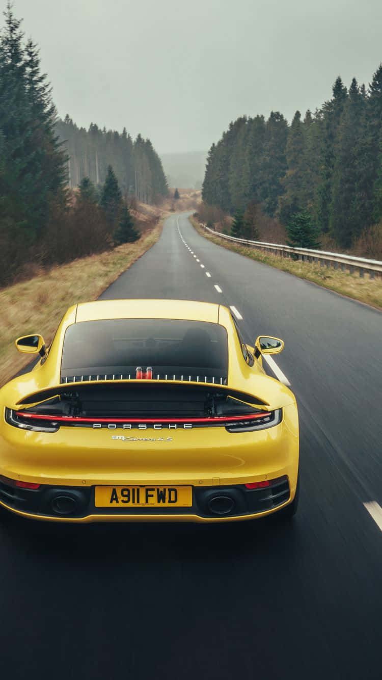 The Rear End Of A Yellow Porsche Cayman Driving Down A Road Background