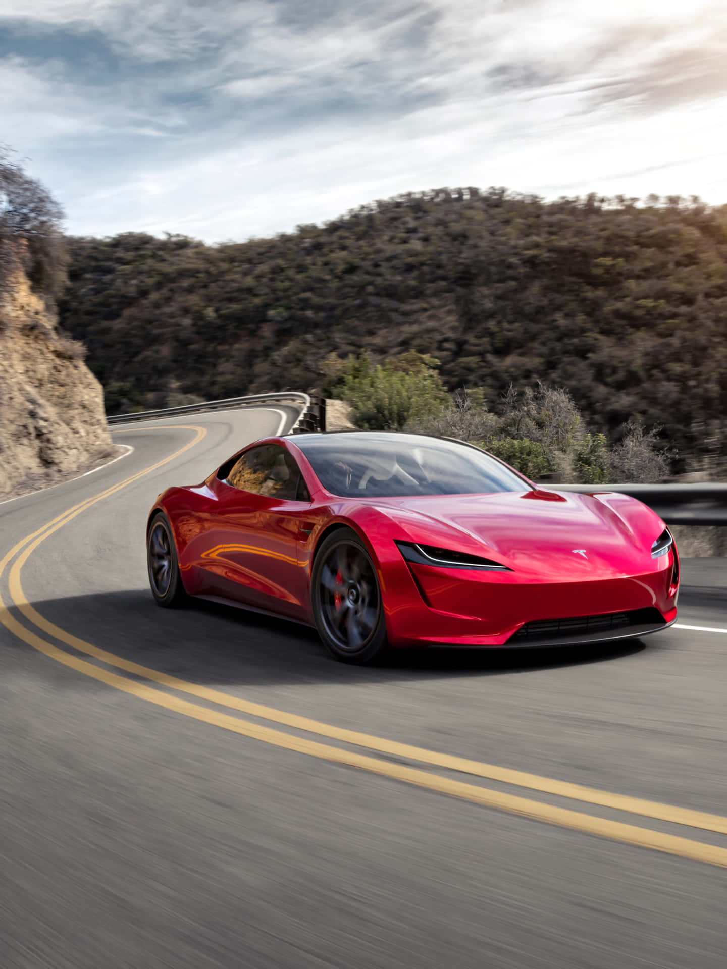 The Red Tesla E-sports Car Is Driving Down A Mountain Road Background