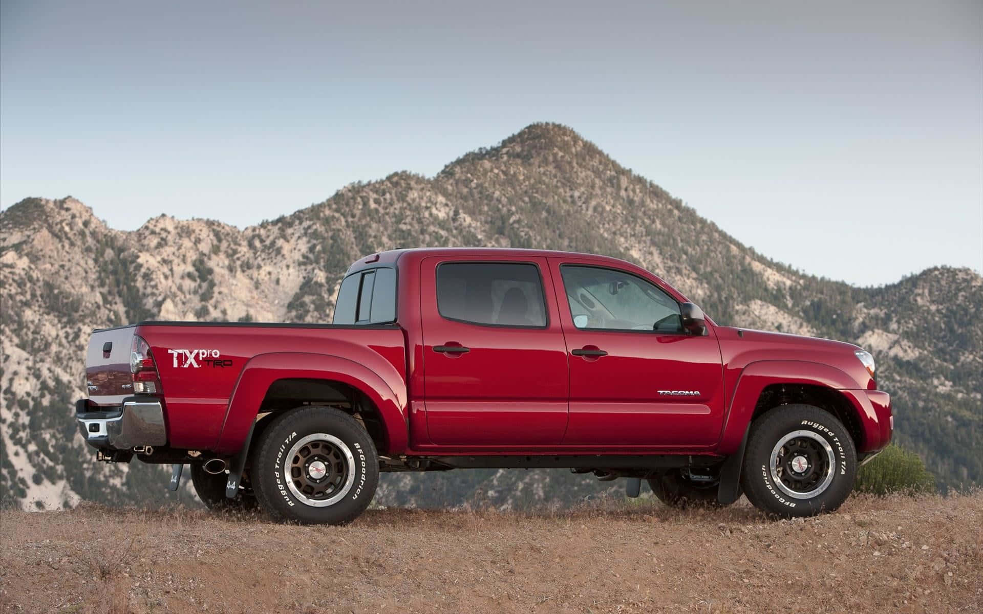 The Red Toyota Tacoma Is Parked In Front Of Mountains Background