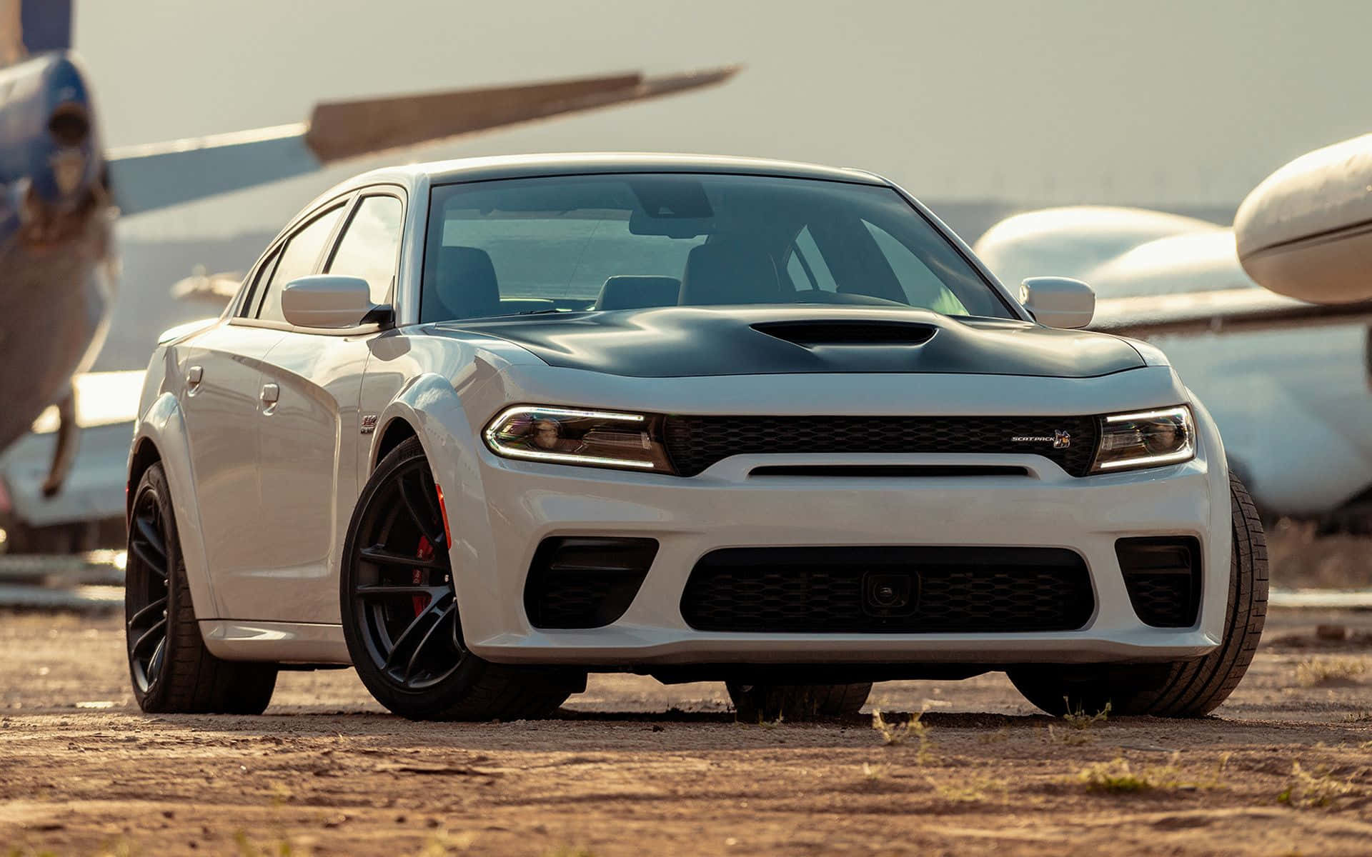 The White Dodge Charger Srt Parked Next To An Airplane Background