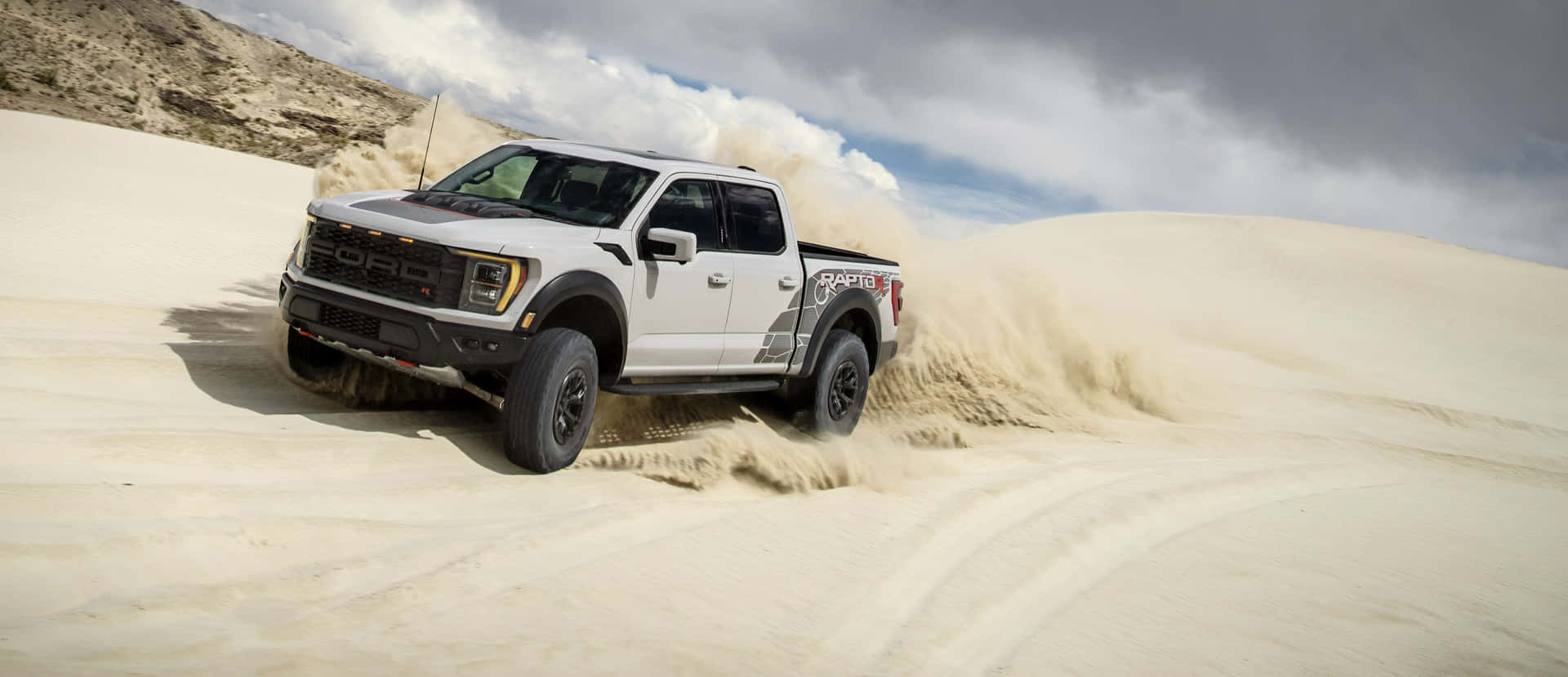 The White Ford F - 150 Raptor Is Driving Through The Sand Dunes Background