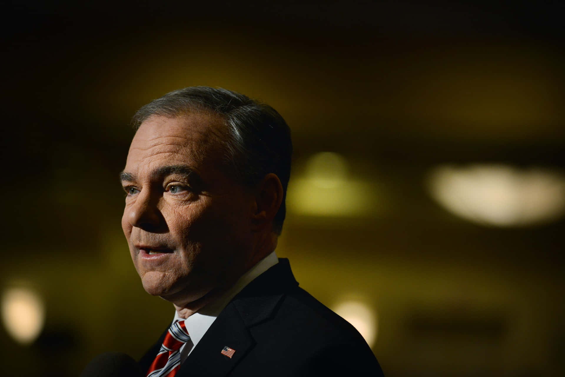 Thoughtful Tim Kaine In A Dimly Lit Room Background