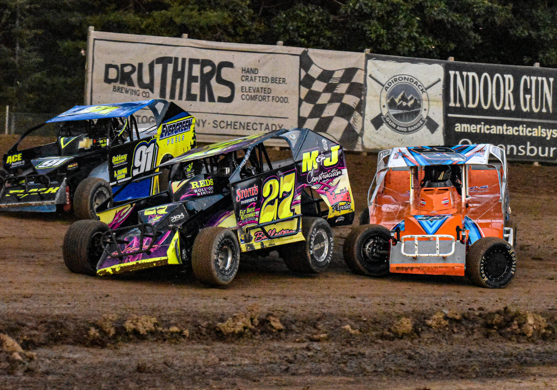 Three Dirt Cars Racing On A Dirt Track Background