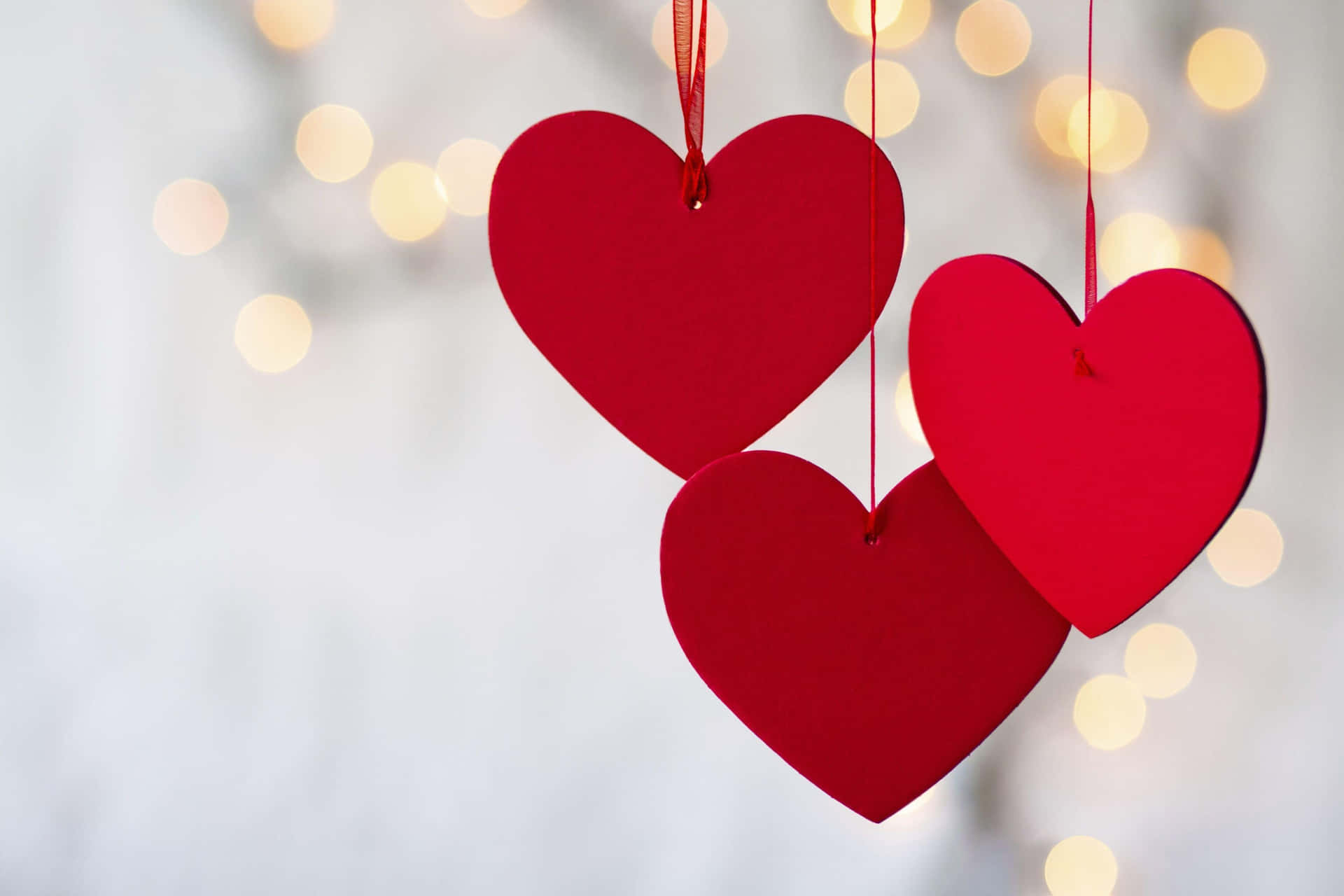 Three Red Hearts Hanging From Strings With Lights Behind Them