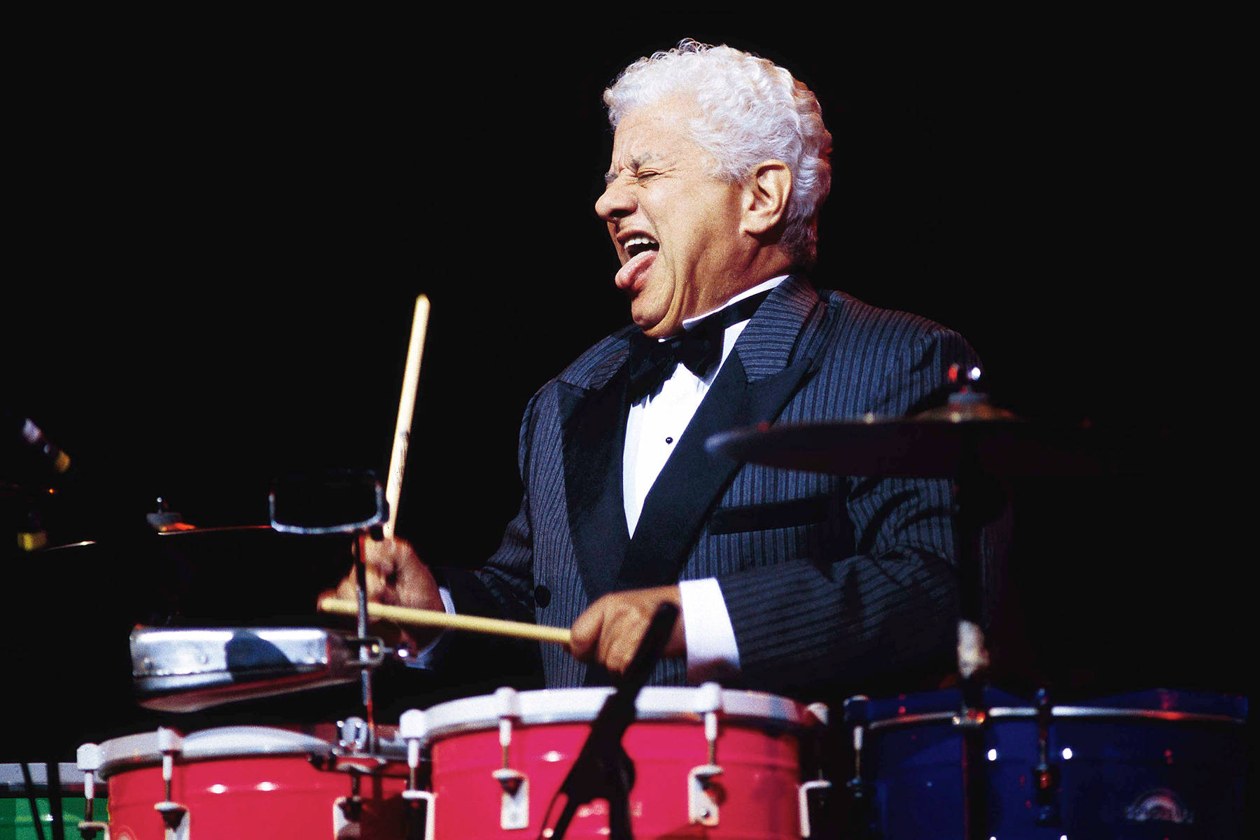 Tito Puente Tongue Out While Playing Drums Background