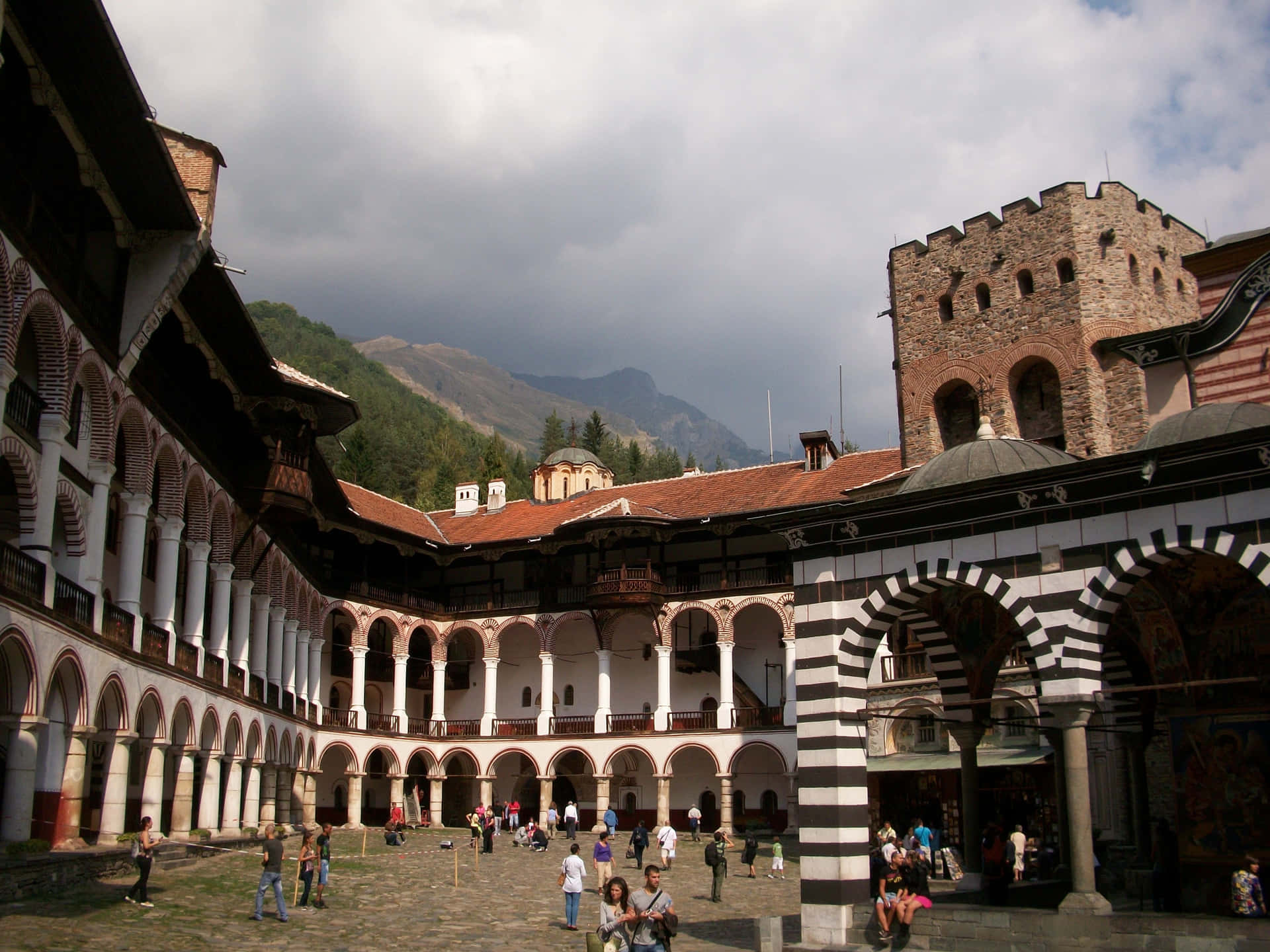 Tourists Exploring The Majestic Rila Monastery In Bulgaria Background