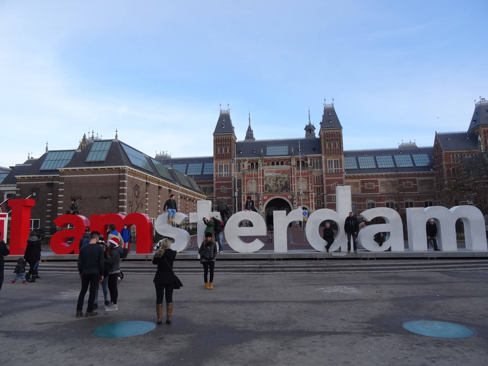 Tourists Posing With The Iconic Amsterdam Sign In Front Of The Prestigious Rijksmuseum. Background