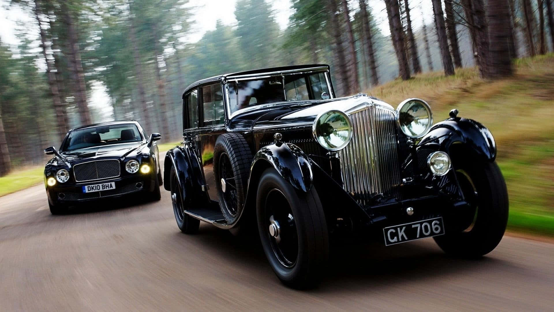 Two Black Cars Are Driving Down A Road In The Woods Background