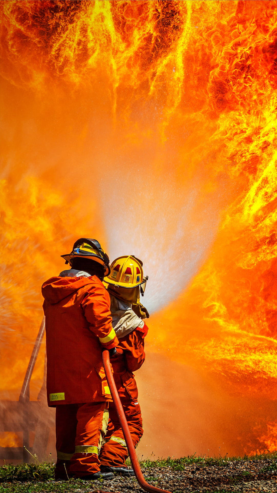 Two Firefighters In Front Of Large Fire Background