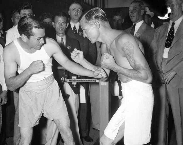 Two Men In Boxing Shorts Fighting In Front Of A Crowd Background