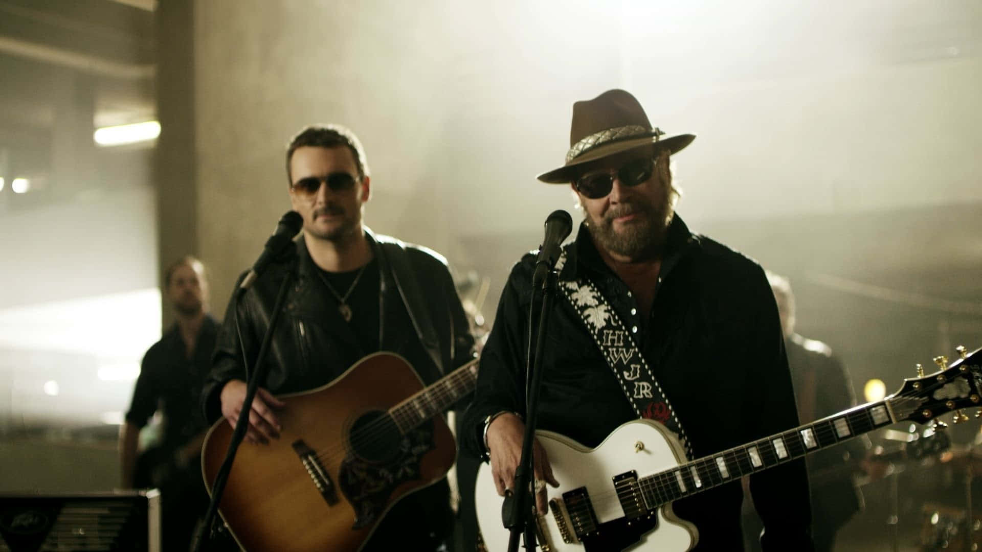Two Men In Hats Playing Guitars In A Room