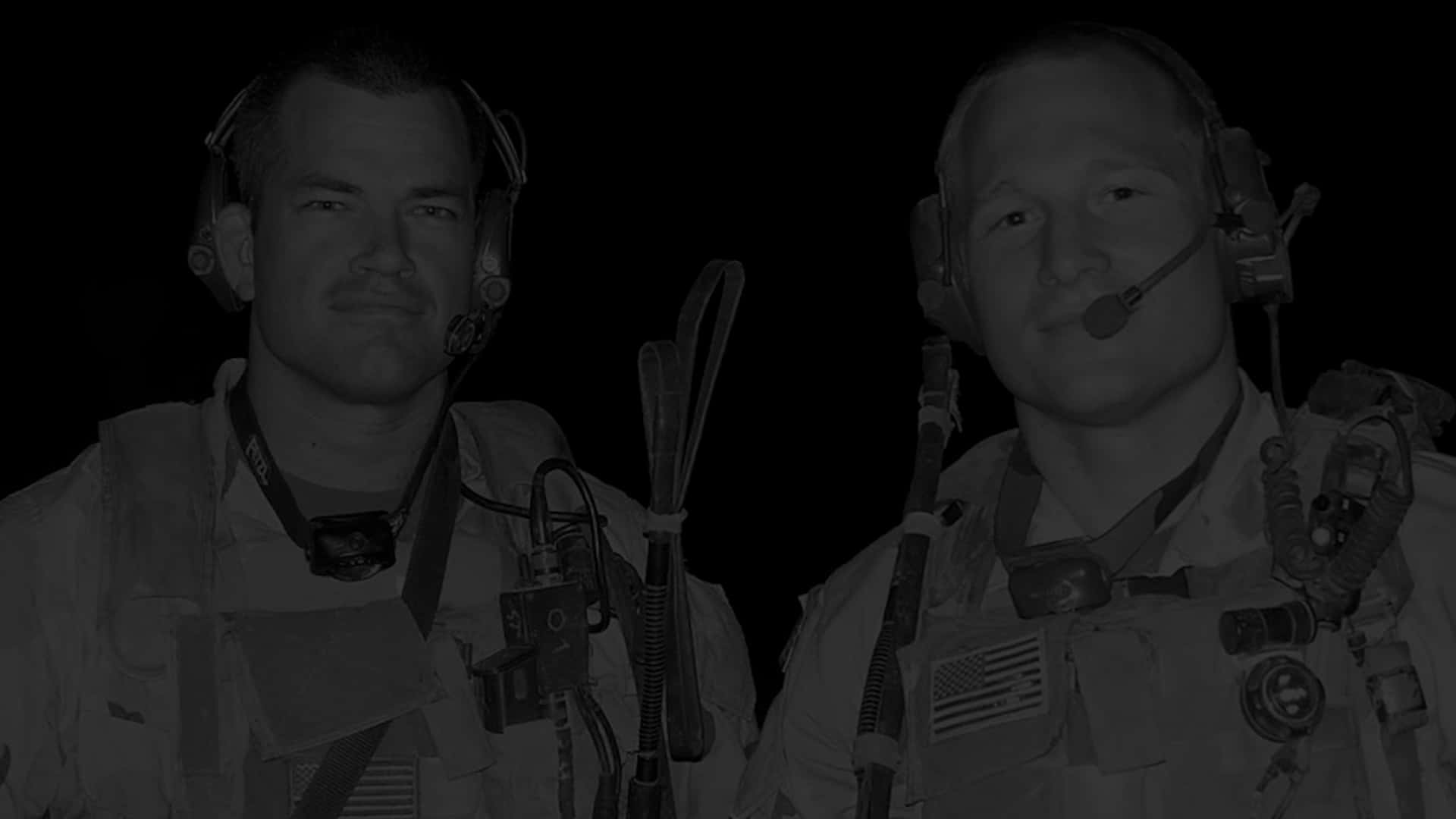 Two Men In Military Uniforms Standing In A Dark Room Background