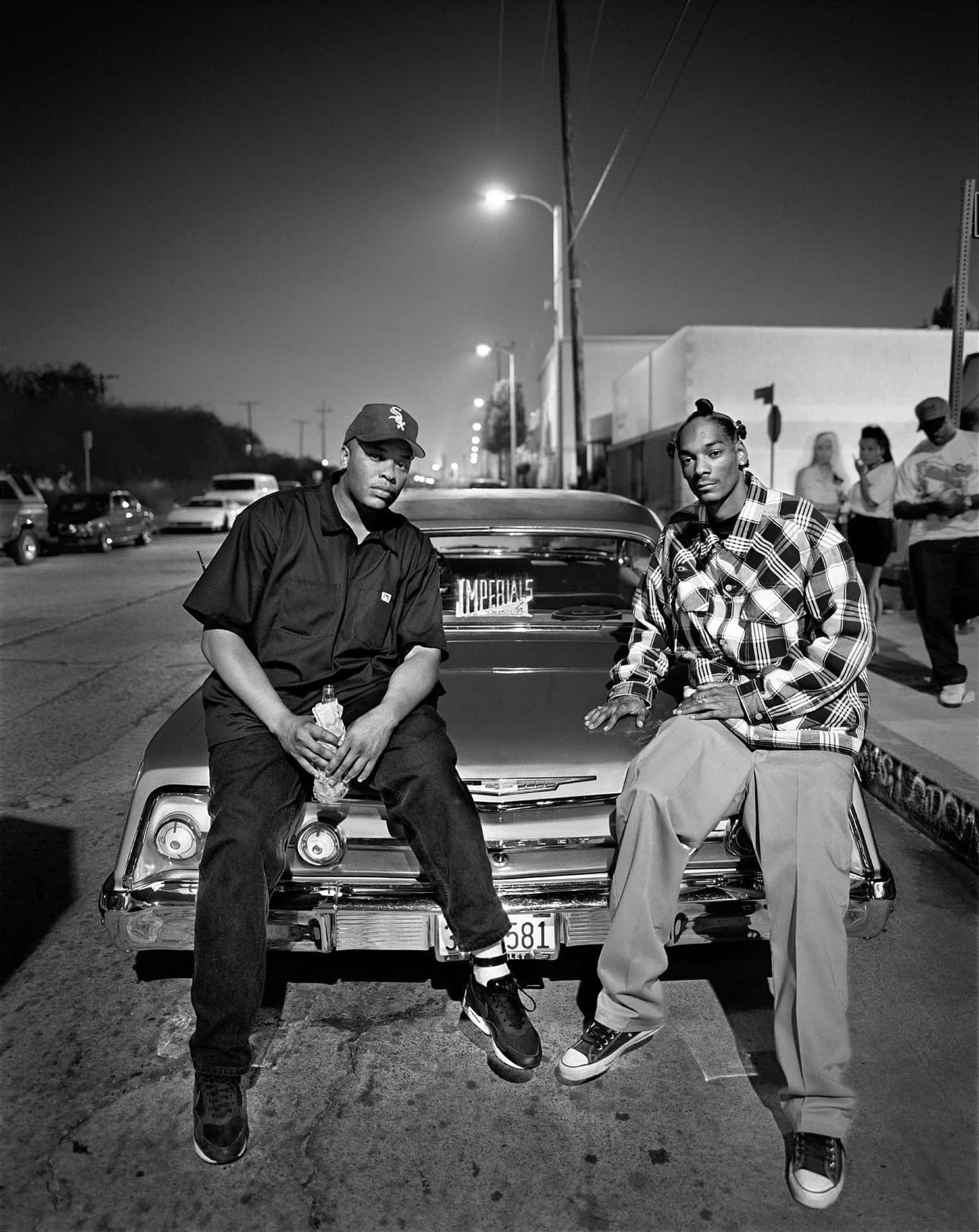 Two Men Sitting On The Side Of A Car At Night Background