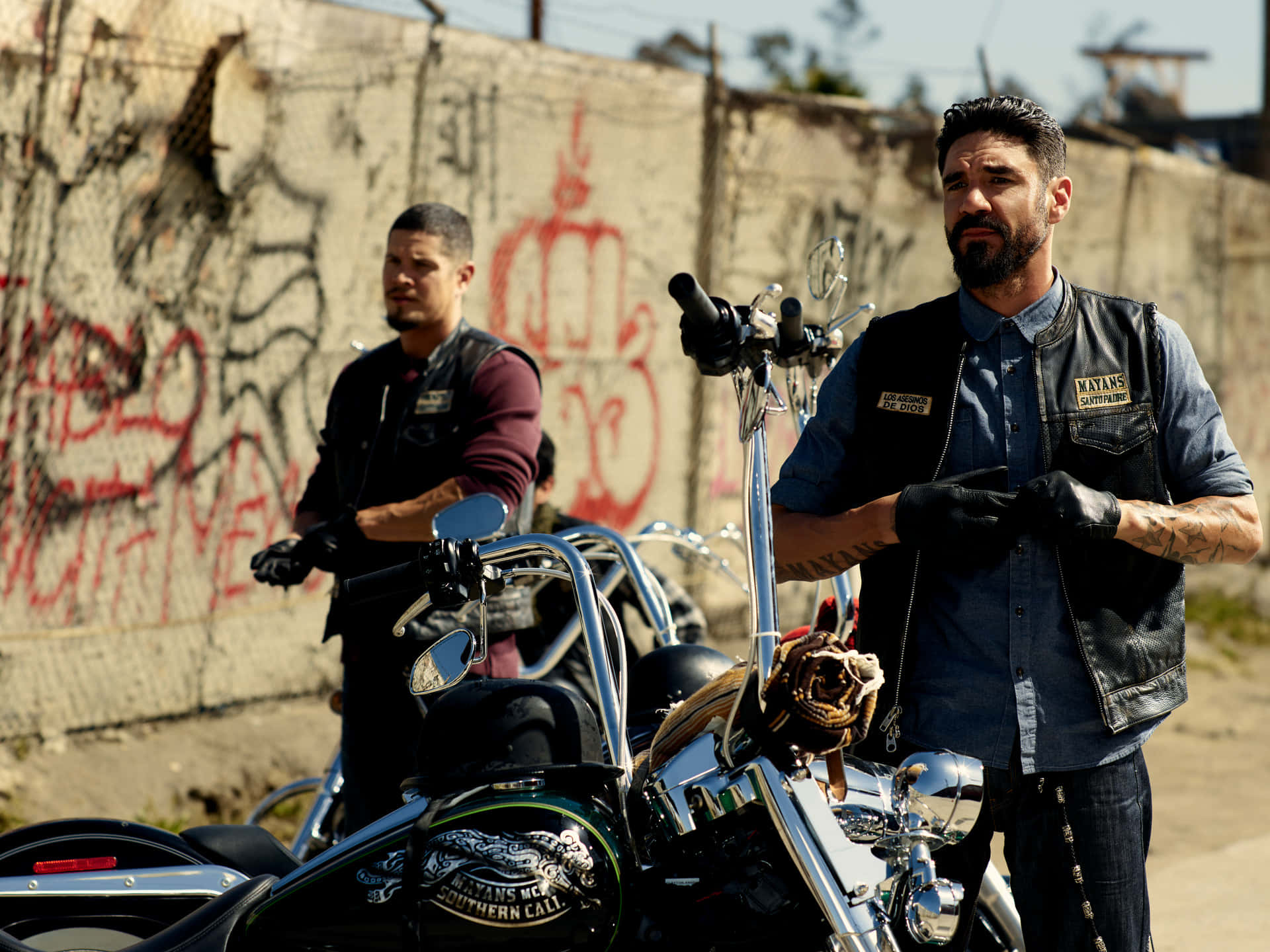 Two Men Standing Next To Motorcycles In Front Of A Wall Background