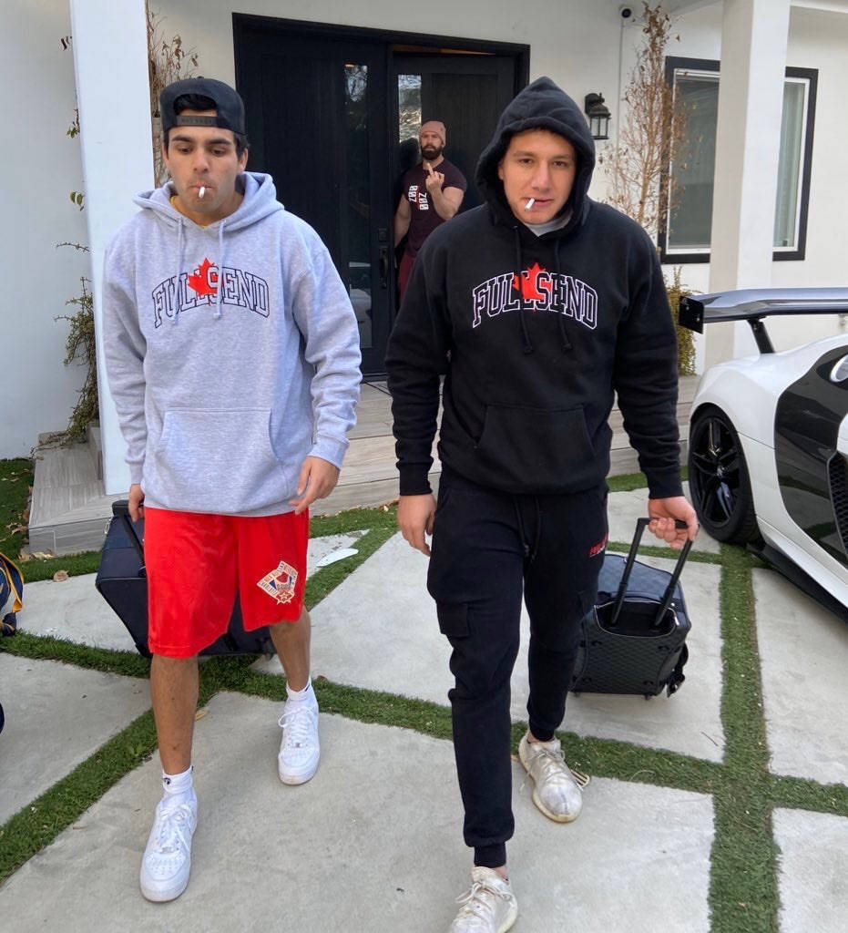 Two Men Walking With Luggage In Front Of A White Car Background