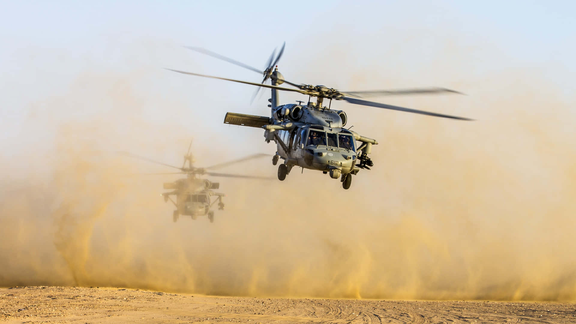 Two Military Helicopters Flying Over A Desert Background