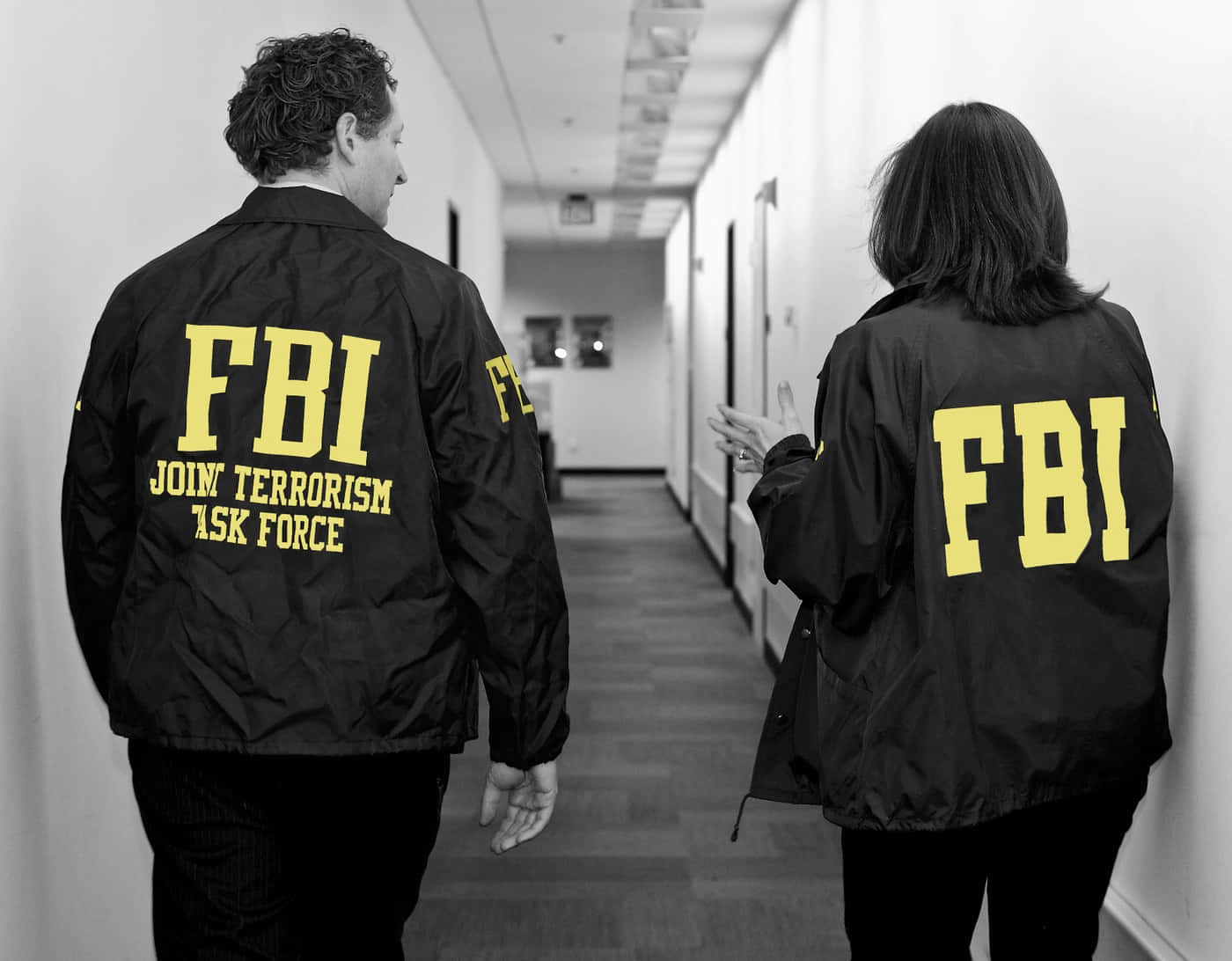 Two People In Fbi Jackets Walking Down A Hallway Background