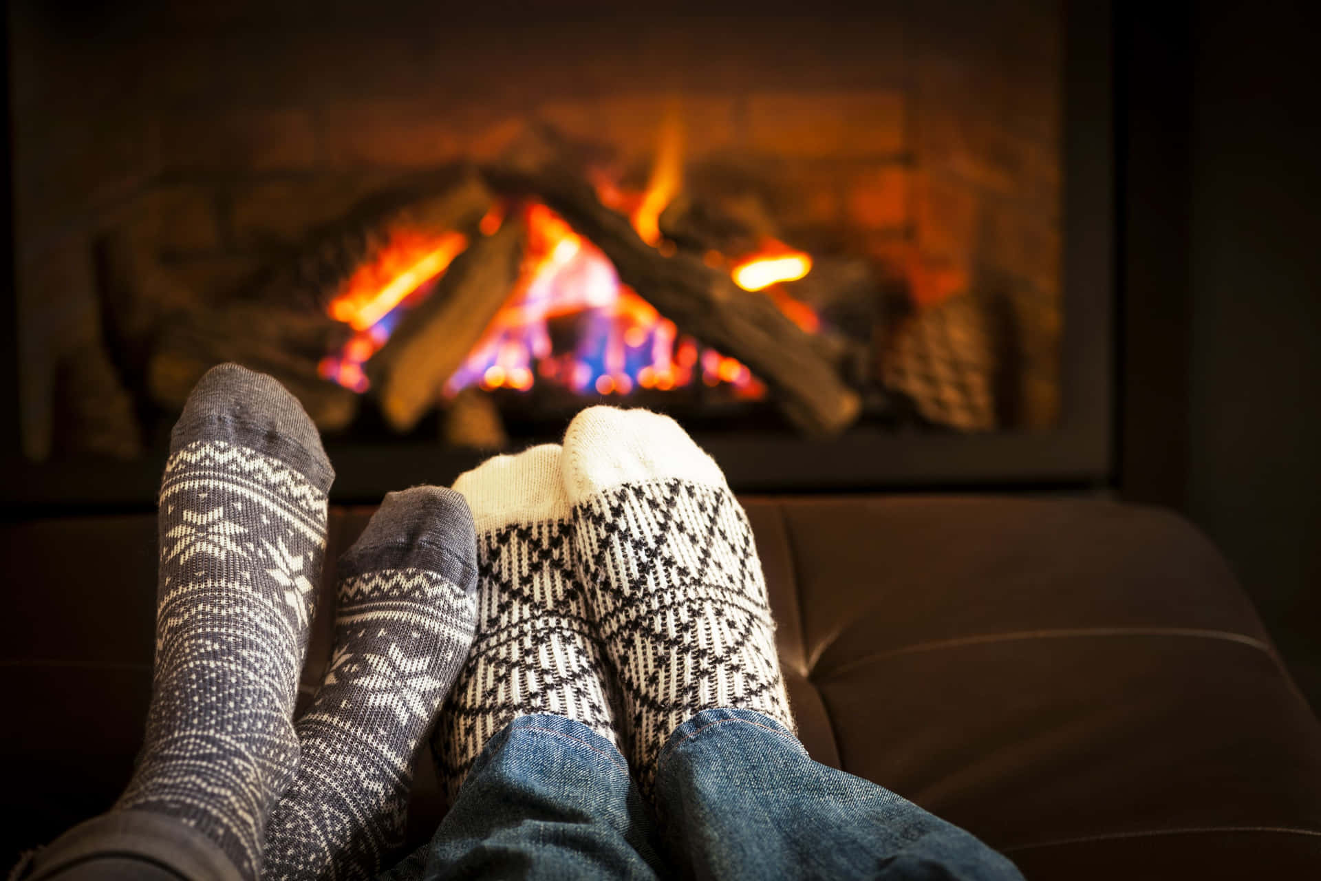 Two People Sitting In Front Of A Fireplace With Their Feet In Socks Background