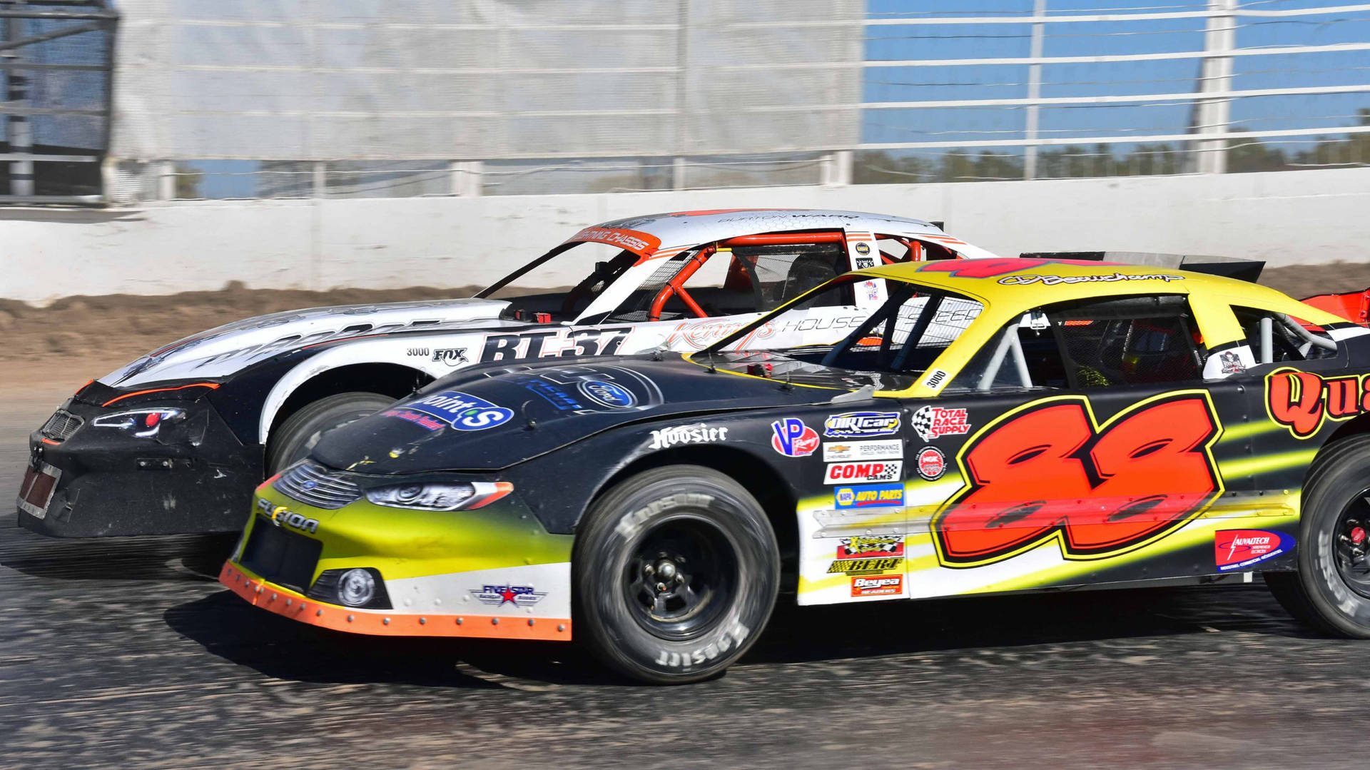 Two Race Cars Racing On A Dirt Track Background