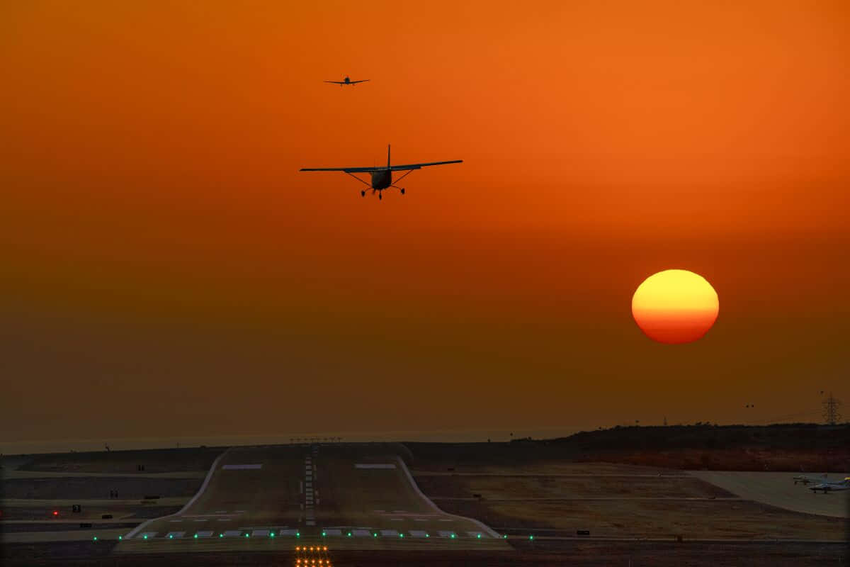 Two Small Airplanes Above Airport Runway Background