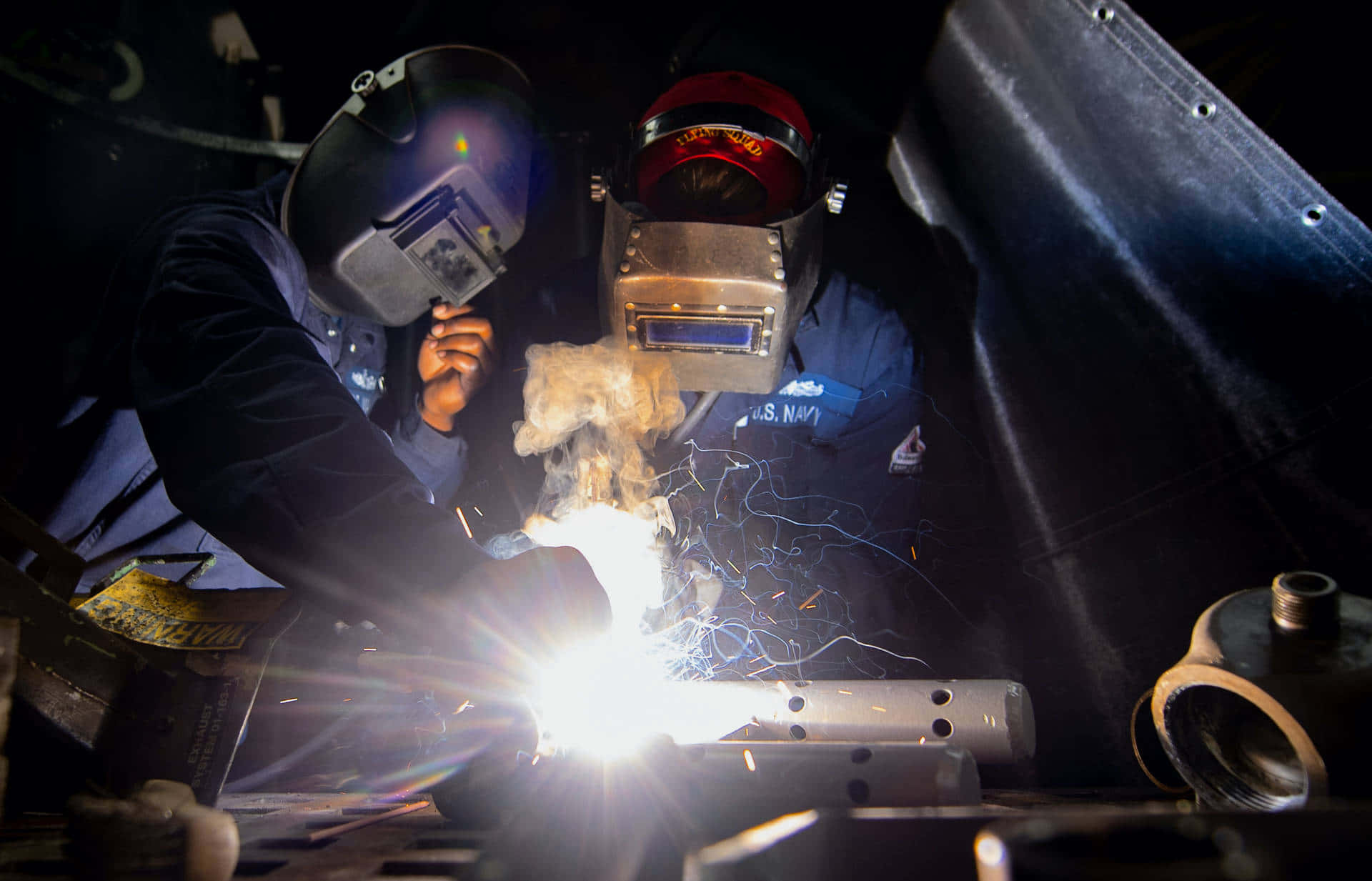 Two Welders Working On A Metal Piece Background