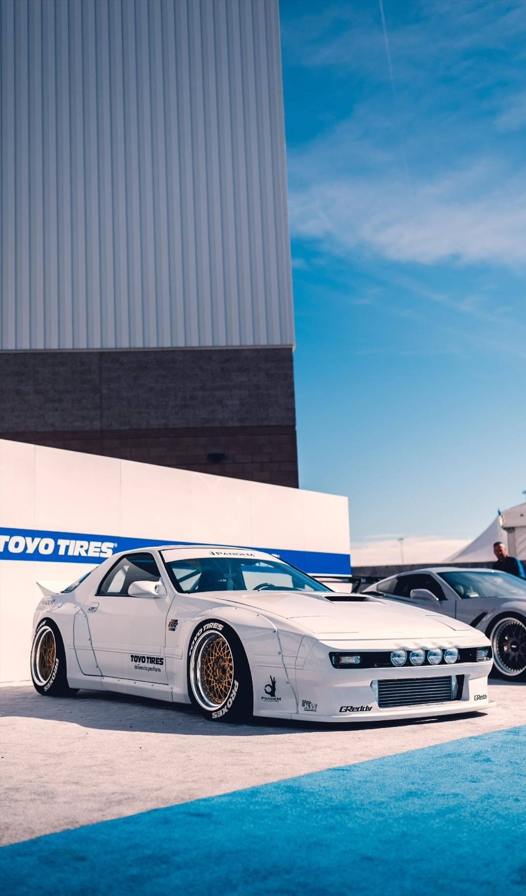 Two White Sports Cars Parked In Front Of A Building Background