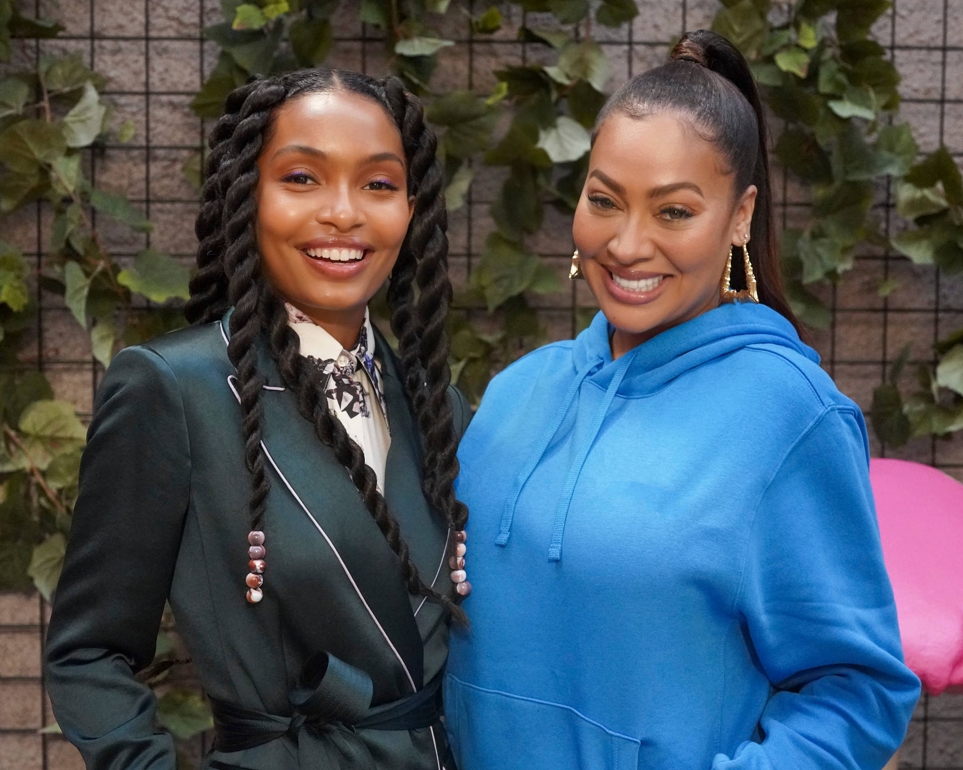 Two Women Standing Next To Each Other In Front Of A Wall Background