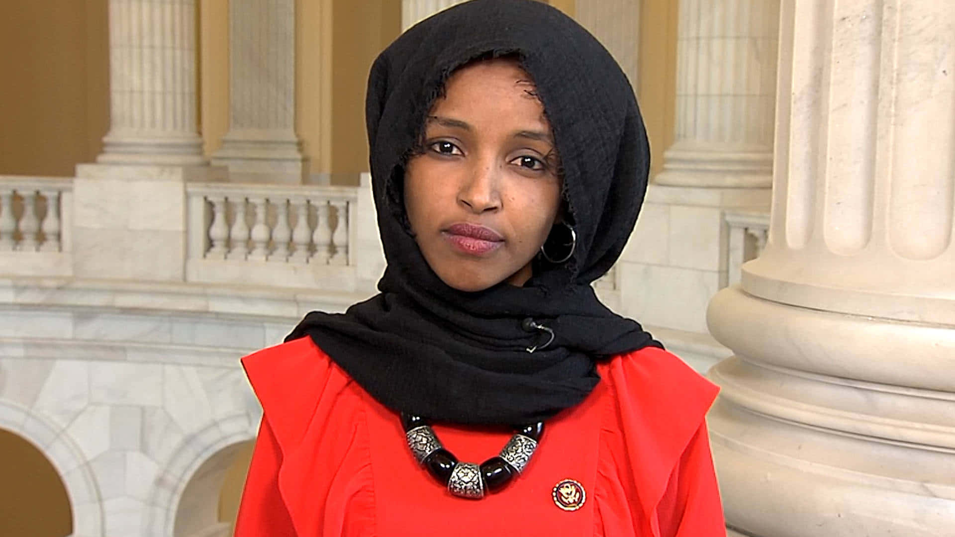 U.s. Representative Ilhan Omar Posing Elegantly In An Orange Dress Background