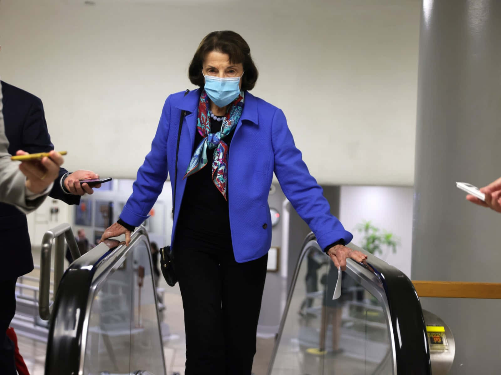 U.s. Senator Dianne Feinstein Wearing A Mask On An Escalator Background