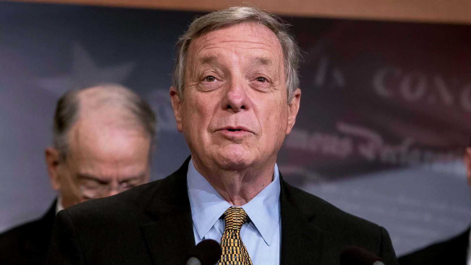 U.s. Senator Richard Durbin Speaking At A Press Conference Background