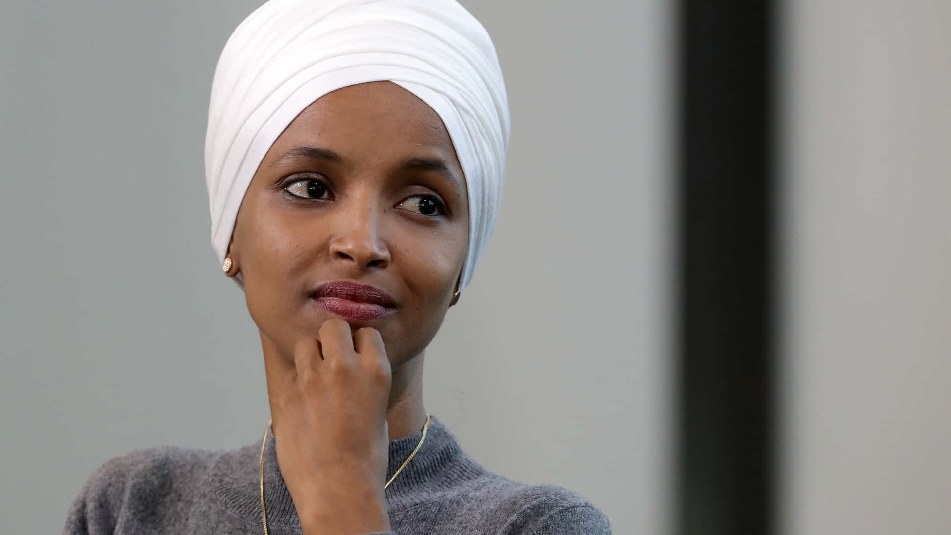 Us Representative Ilhan Omar Posing With A Contemplative Expression Background