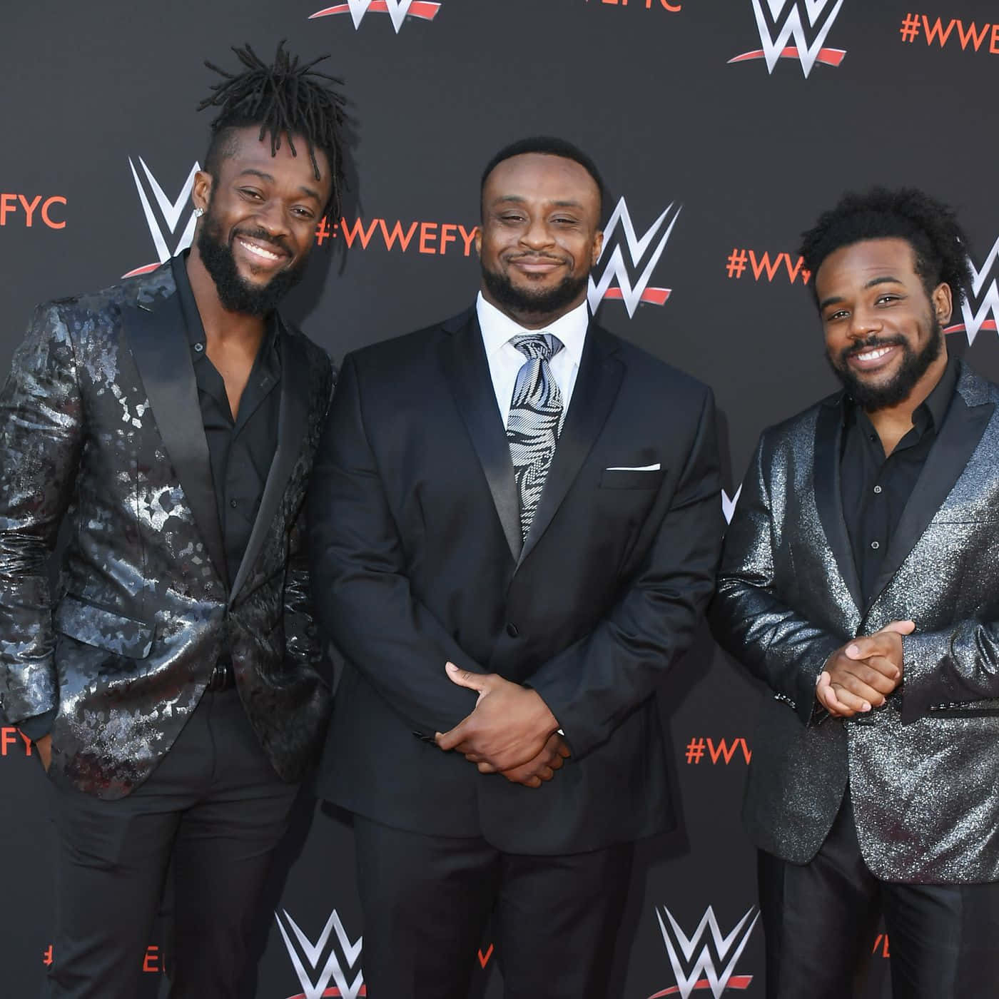 Vibrant Image Of Wwe Superstar Kofi Kingston, Posing With The Big E And Xavier Woods. Background