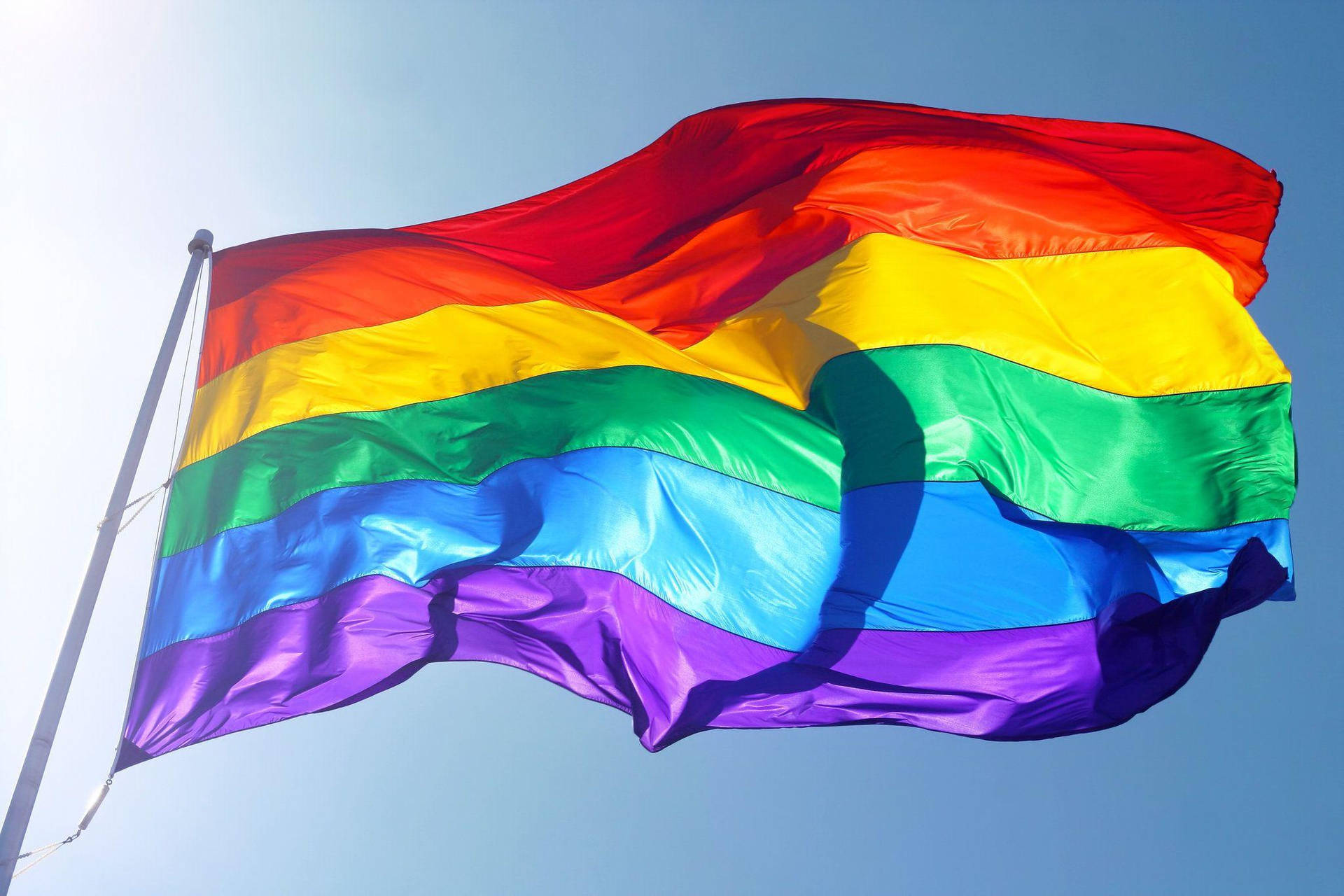 Vibrant Pride Flag Fluttering Under Sunlight Background