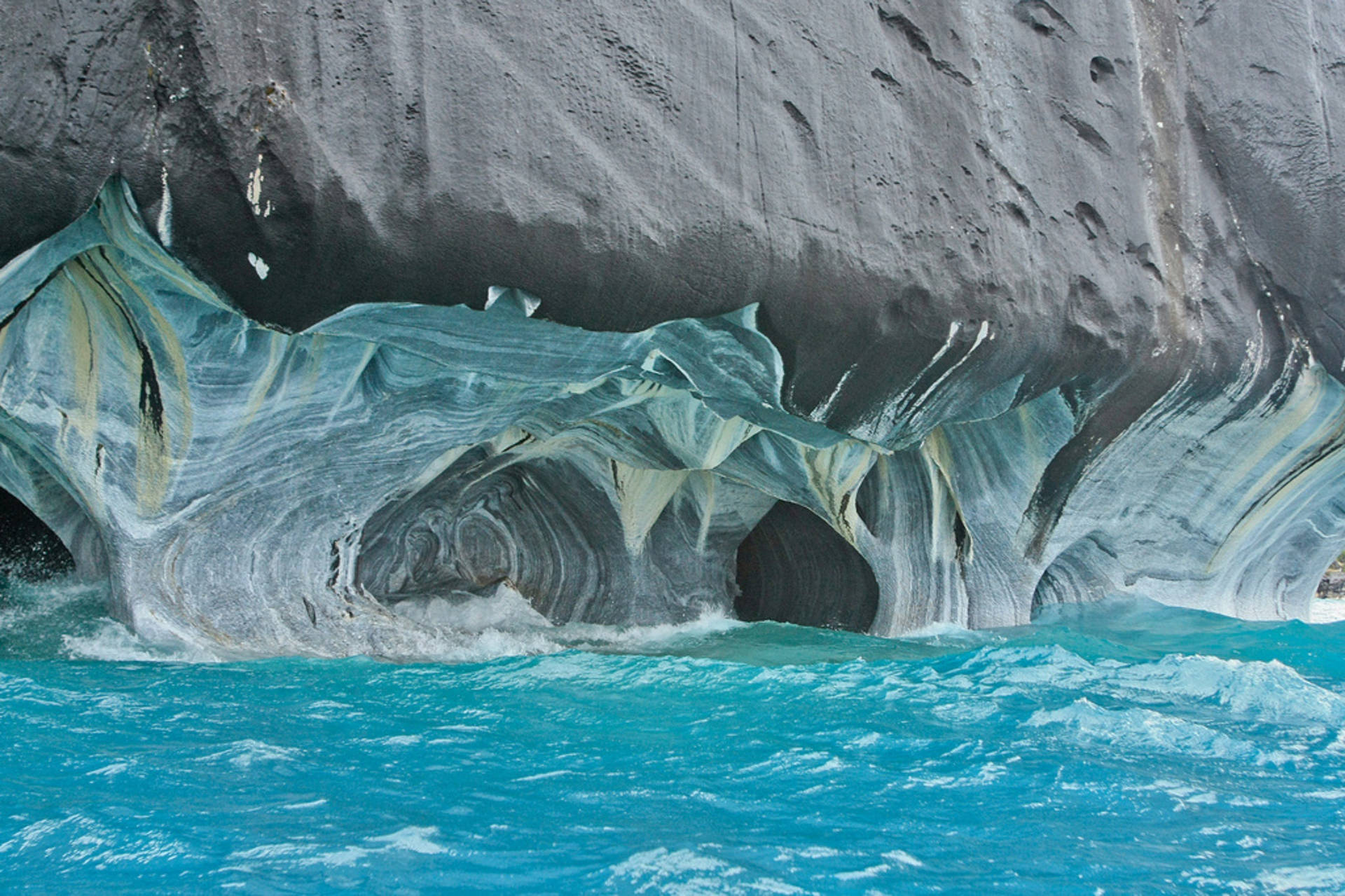 Visitors Admire The Stunning Blue And Gold Marble Formations Of Marble Caves, Chile Background